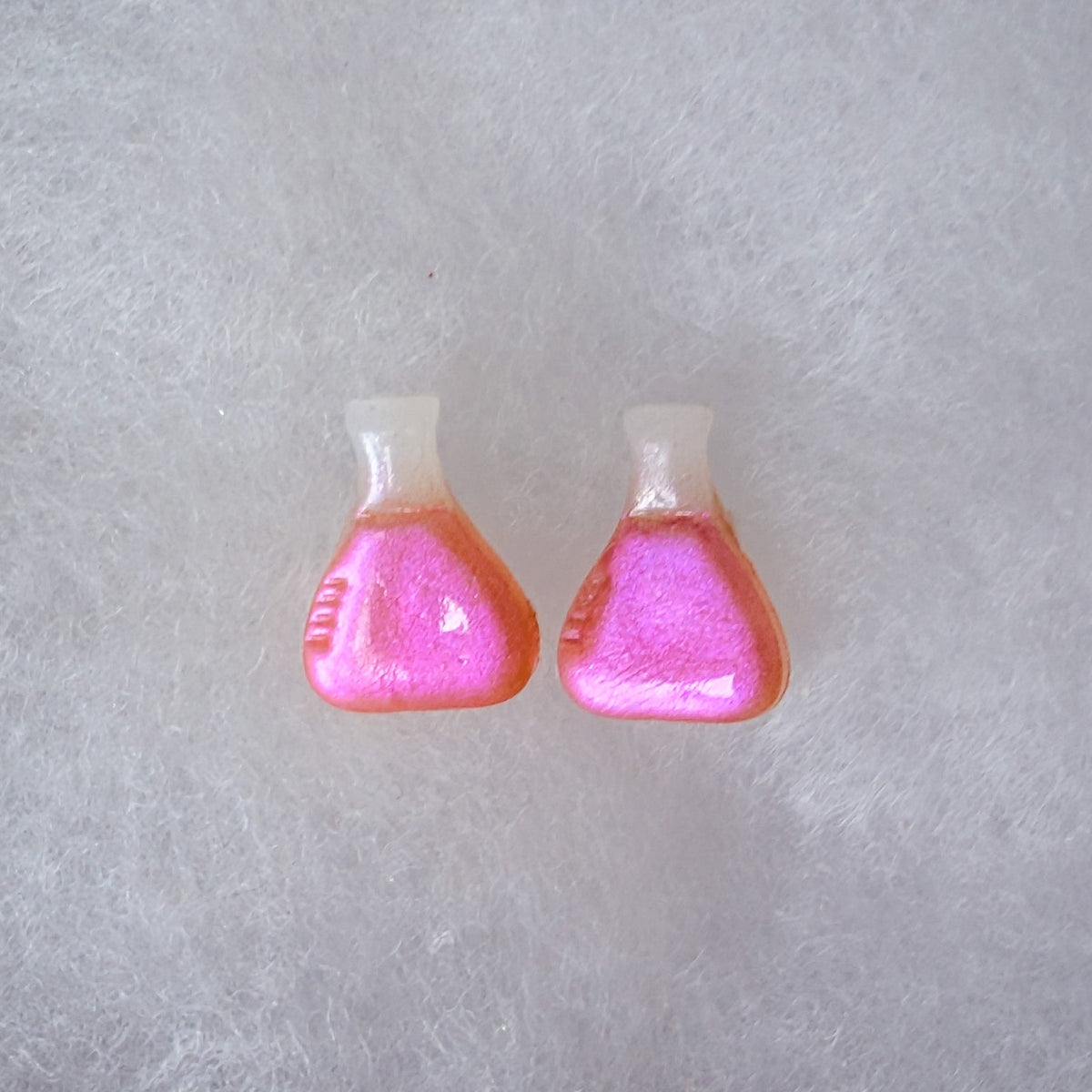 A pair of beaker shaped stud earrings with a translucent top and a glittery magenta to purple colorshift finish.