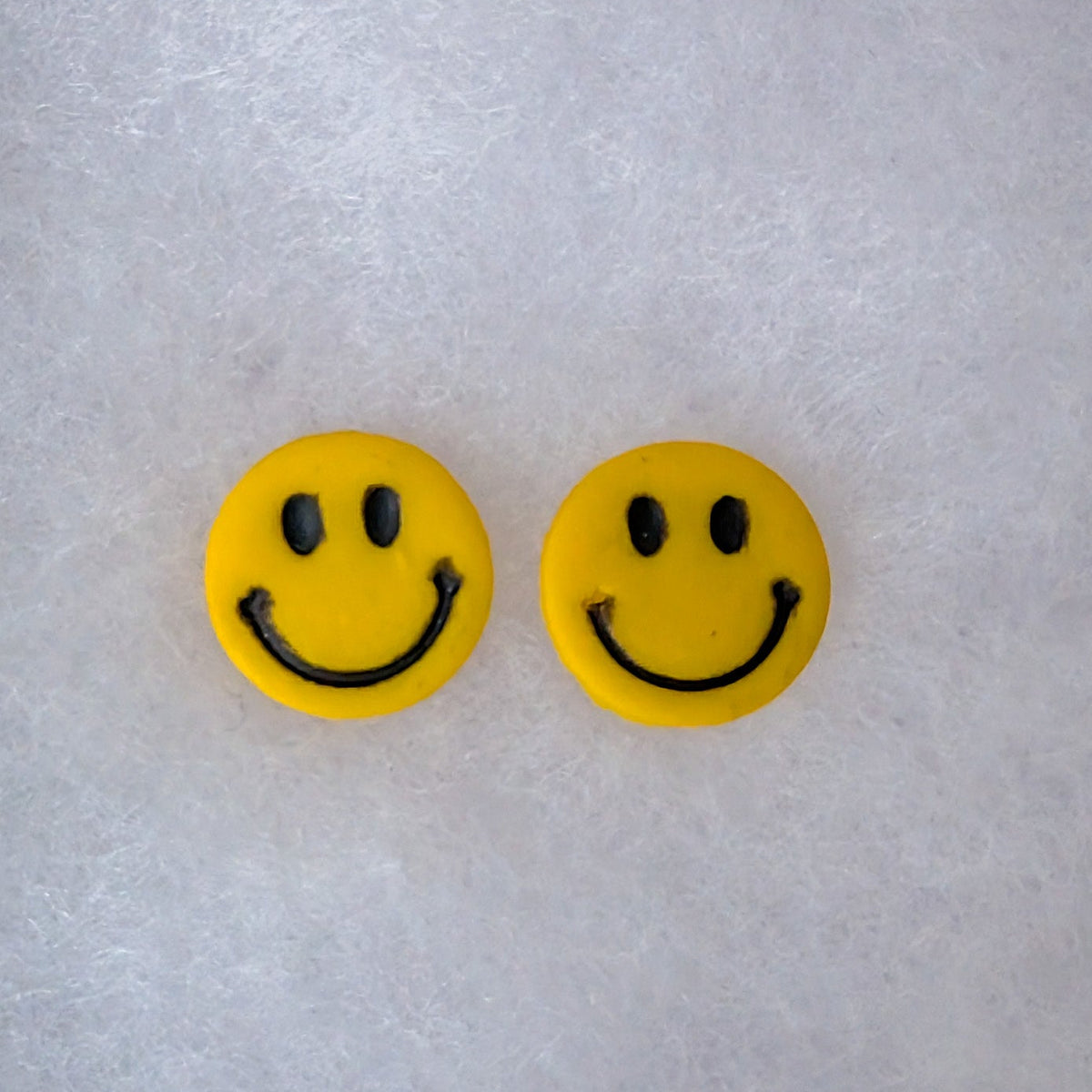 A pair of yellow smiley face stud earrings with black eyes and curved smiles.