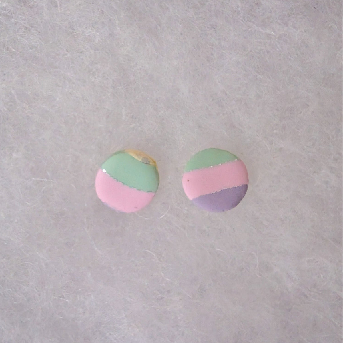 A pair of round stud earrings with a pastel three-color design of pink, mint green, and lavender purple with silver accents