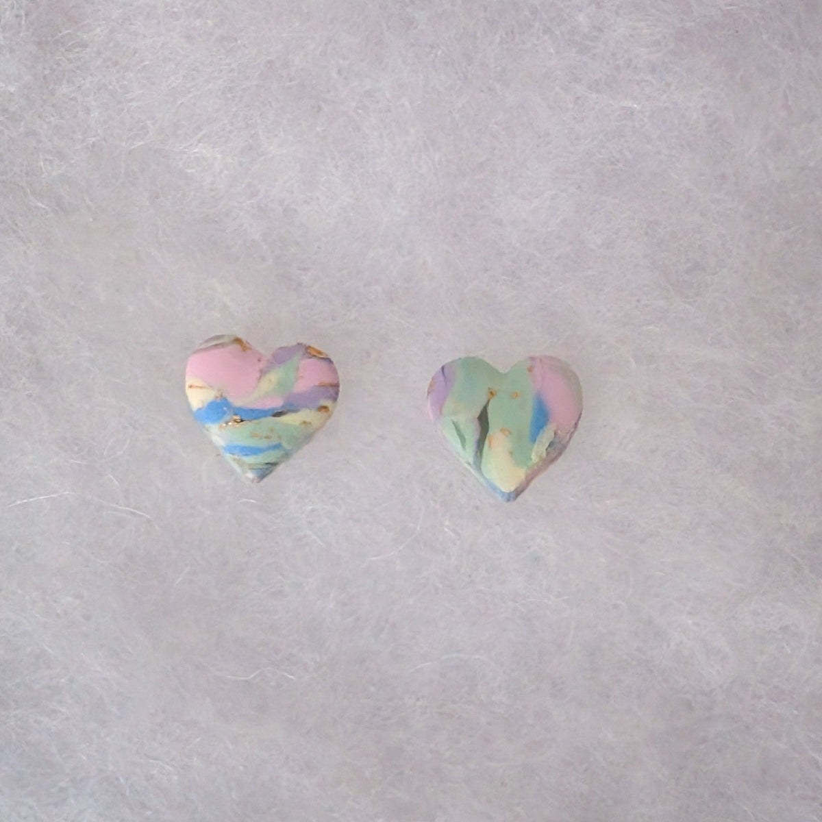 Two small heart-shaped stud earrings with a pastel marbled pattern of pink, blue, green, and yellow with gold accents