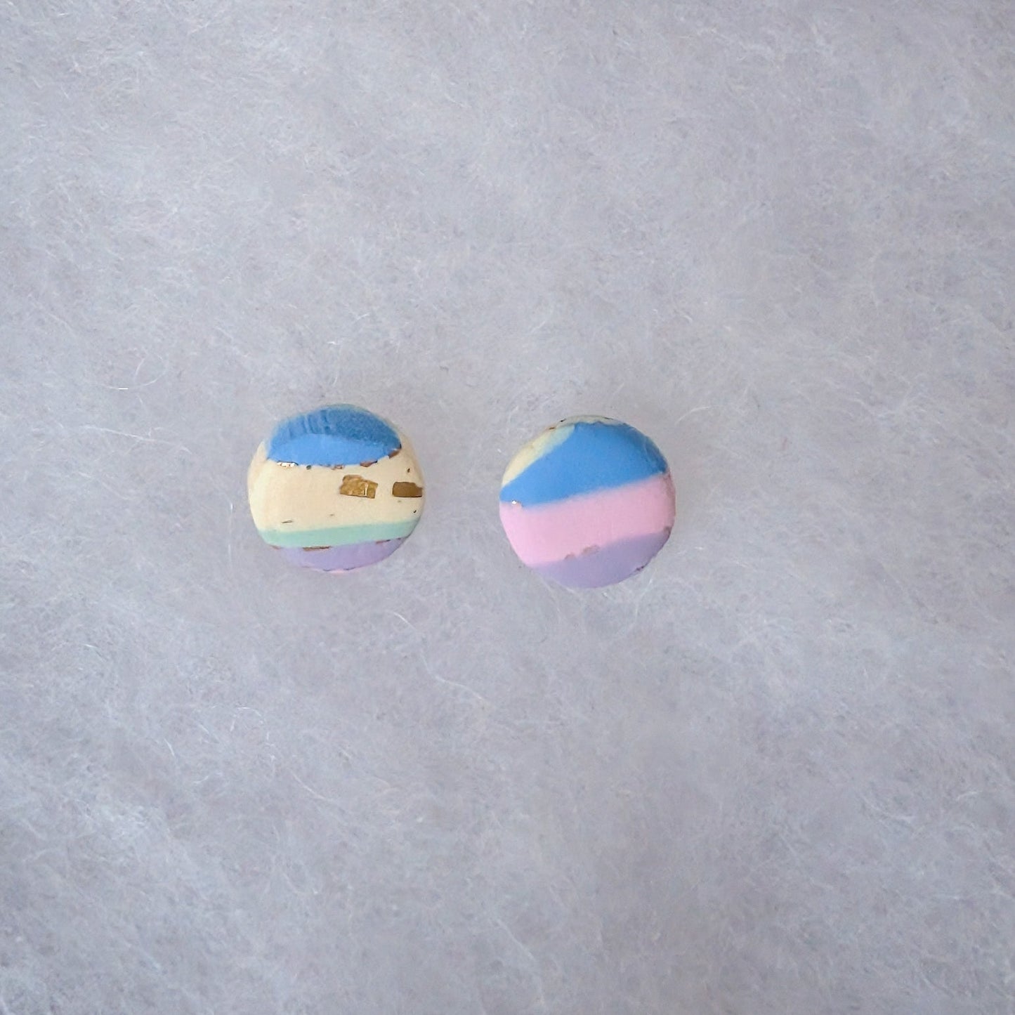 Two small circle stud earrings with pastel stripes in blue, pink, purple, and cream and gold accents