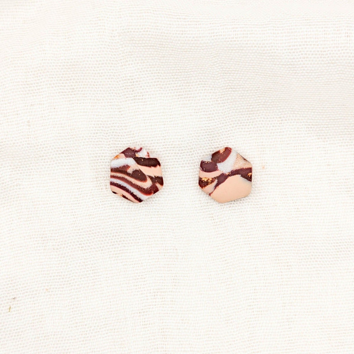 Close-up of geometric hexagon polymer clay stud earrings with brown, cream, and copper marbling