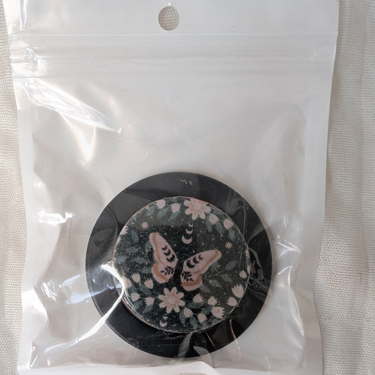 Packaged black MagSafe phone grip featuring a dusty rose moth with floral and moon phase details