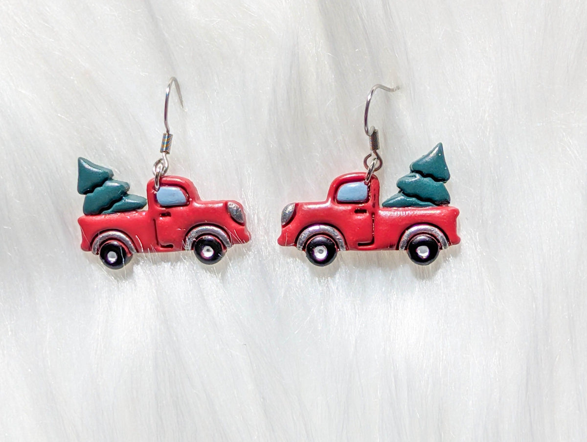 Close-up of handmade red pickup truck earrings carrying evergreen Christmas trees