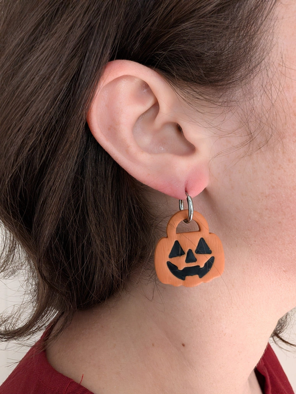 Orange jack-o-lantern trick-or-treat candy pail earring worn on ear