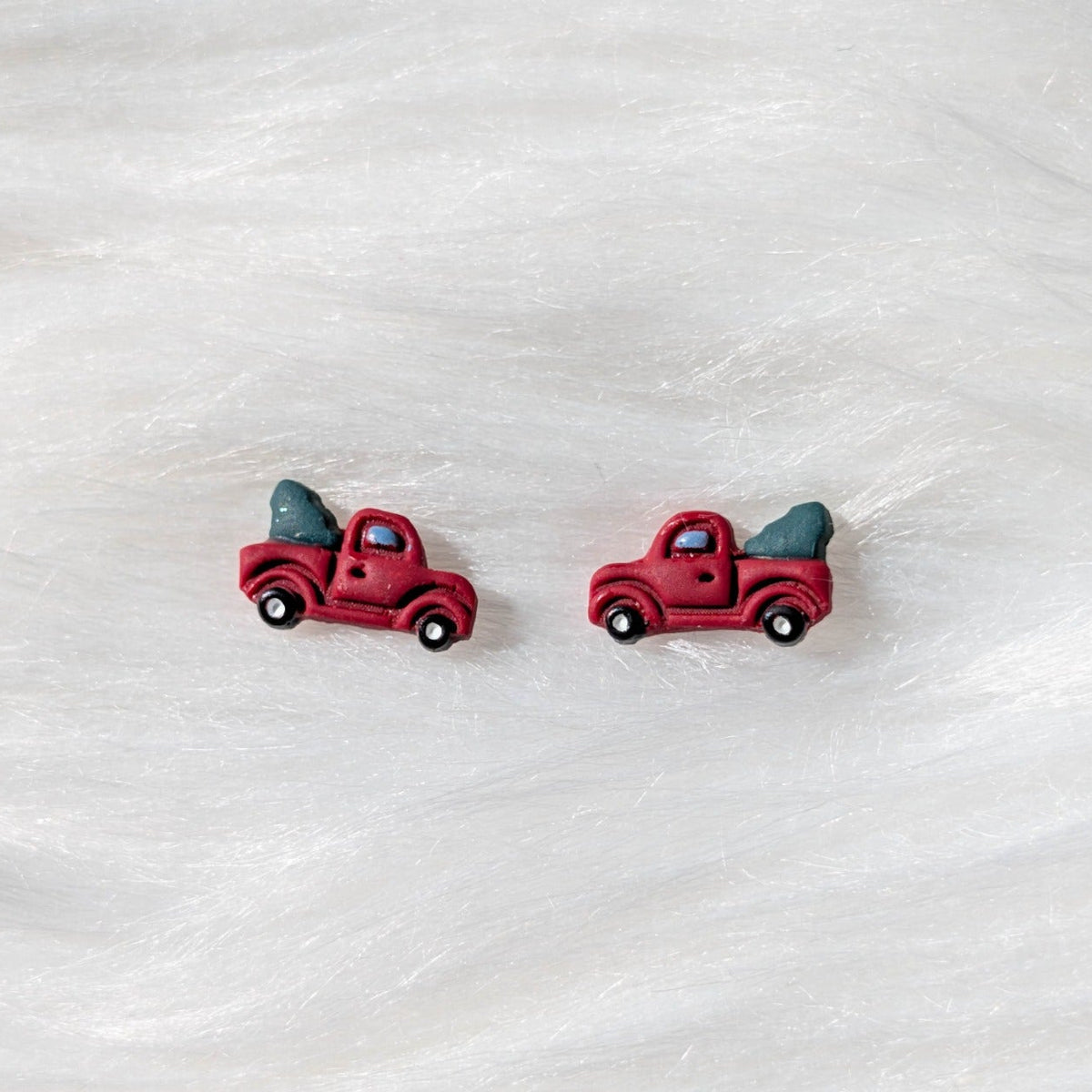 Close-up of miniature vintage red truck stud earrings carrying green Christmas trees