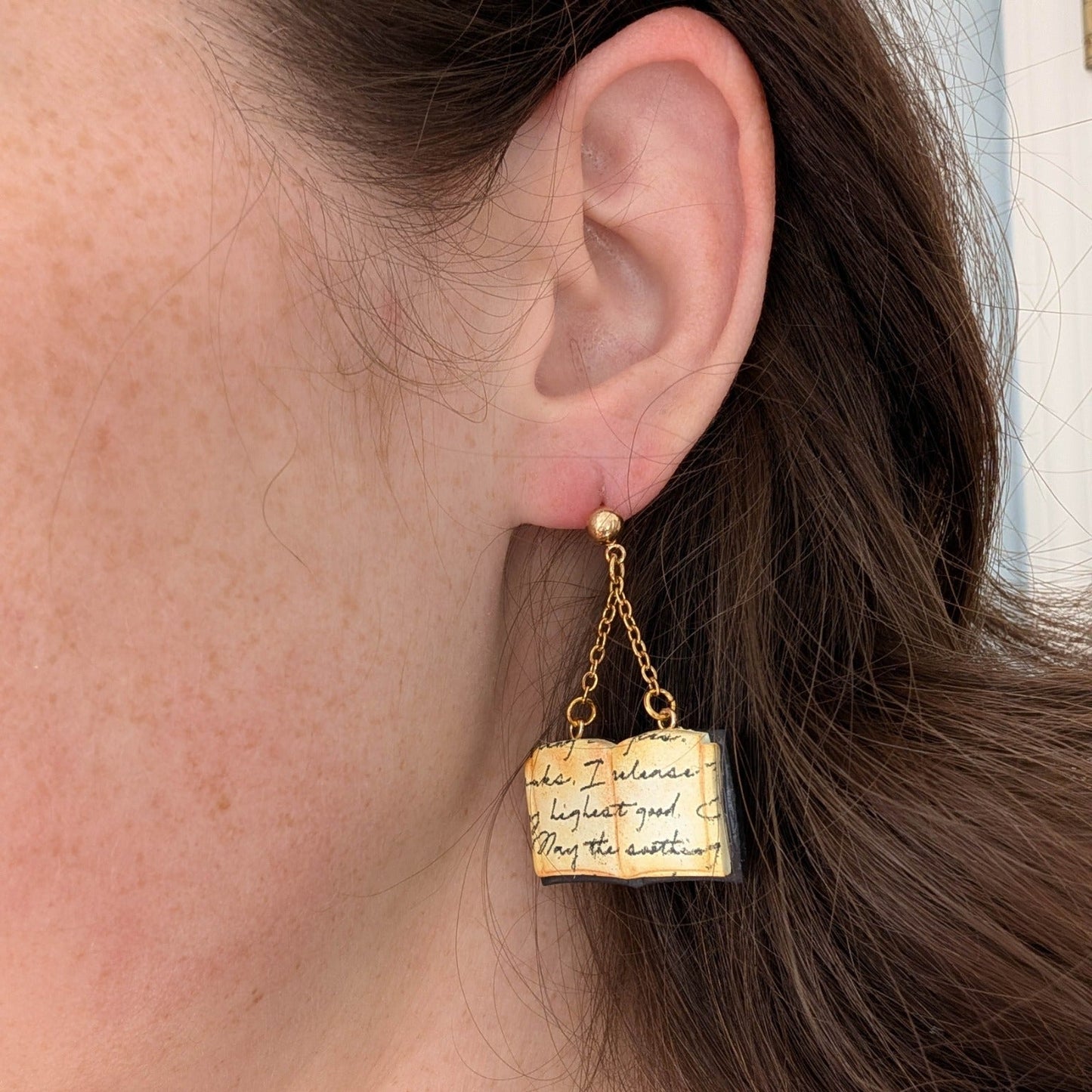 Open spellbook earring with aged handwritten pages and gold hardware worn on ear