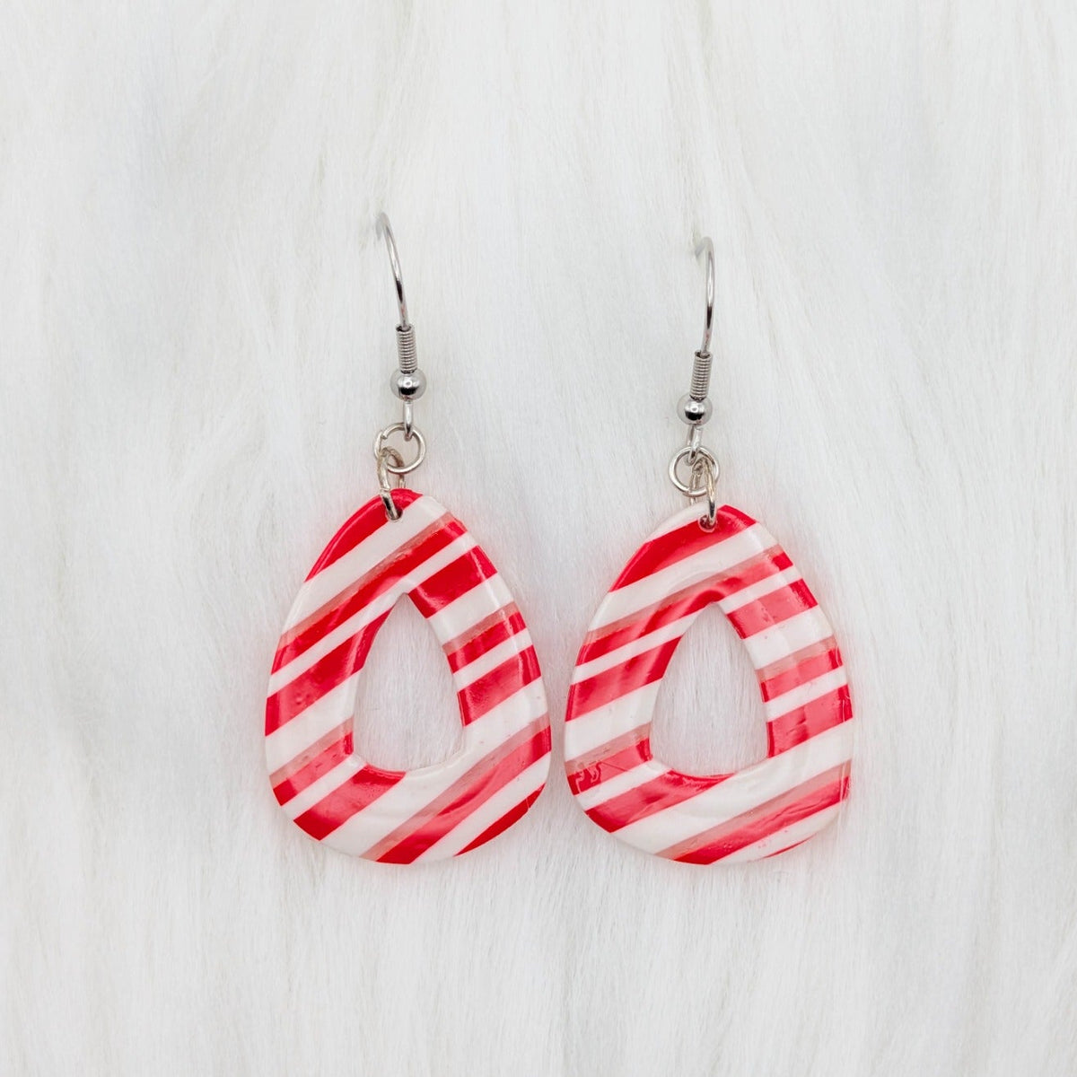 Rounded candy cane striped dangle earrings in red, white, and translucent clay.
