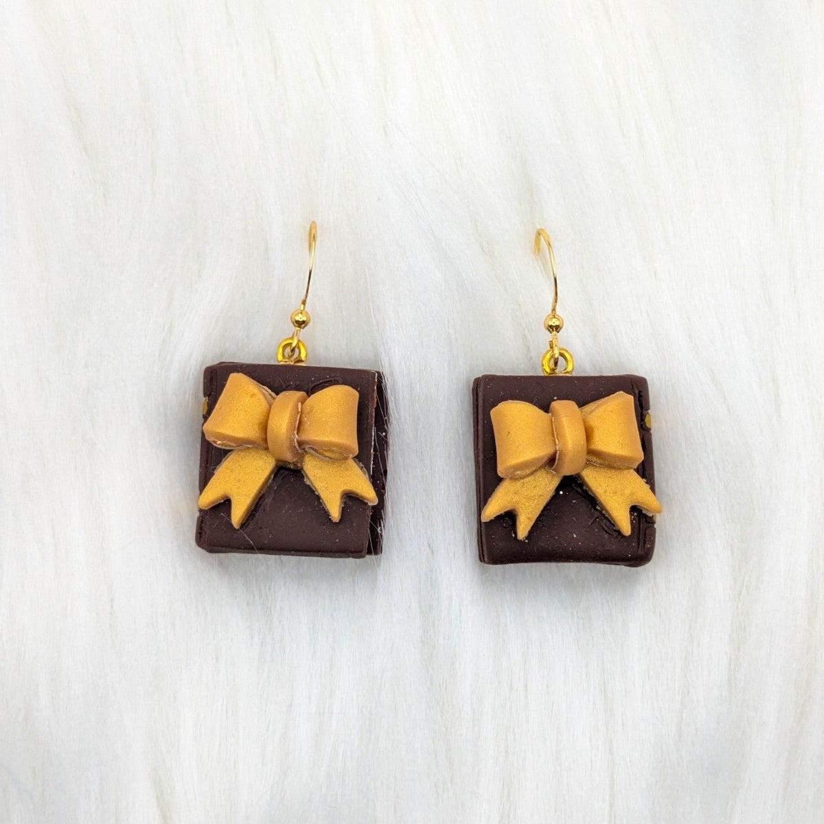 Dark brown miniature book earrings decorated with a gold bow, with gold-tone hooks.