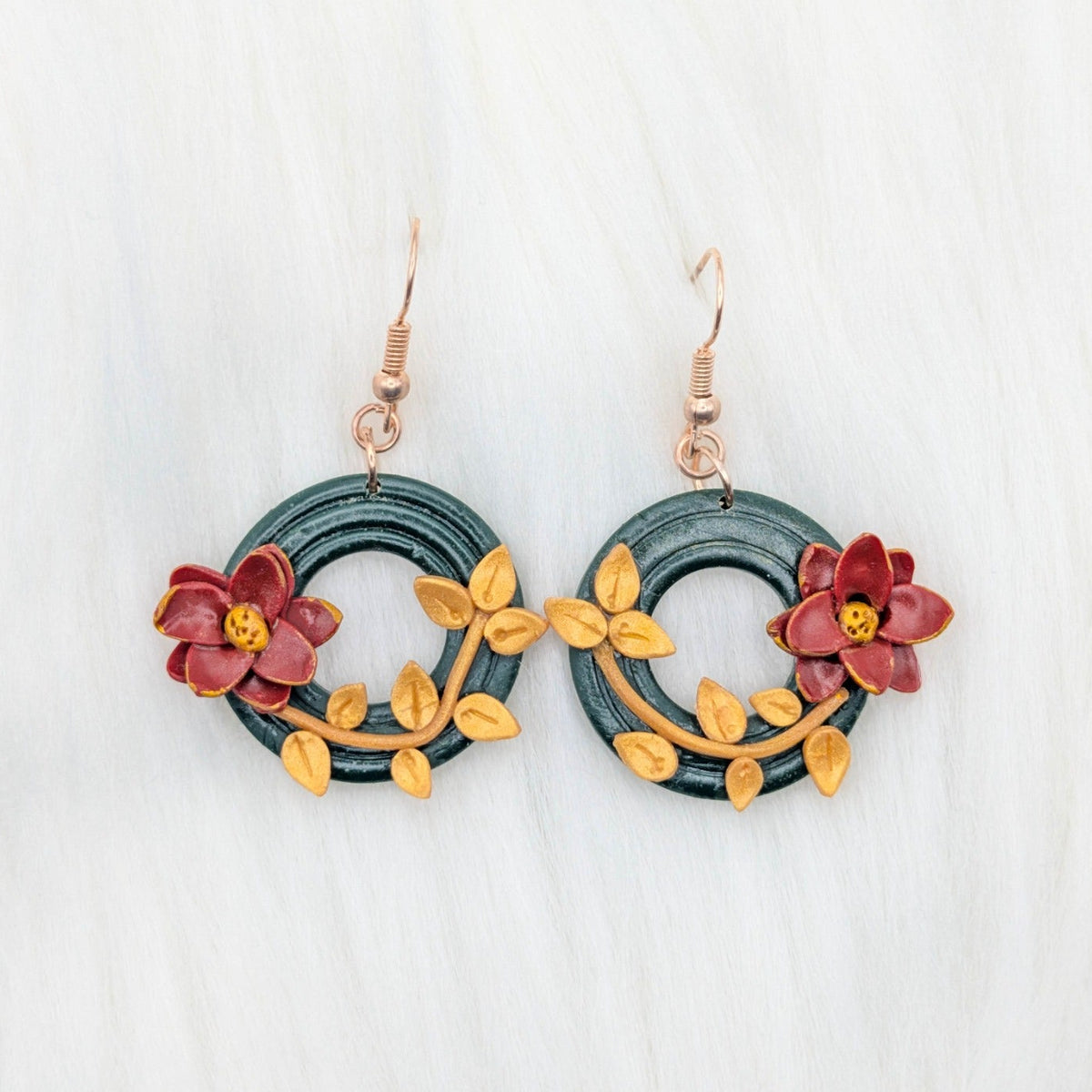 Two handmade poinsettia wreath dangle earrings with green wreaths, gold leaves, red flowers, and gold-plated stainless steel hooks.