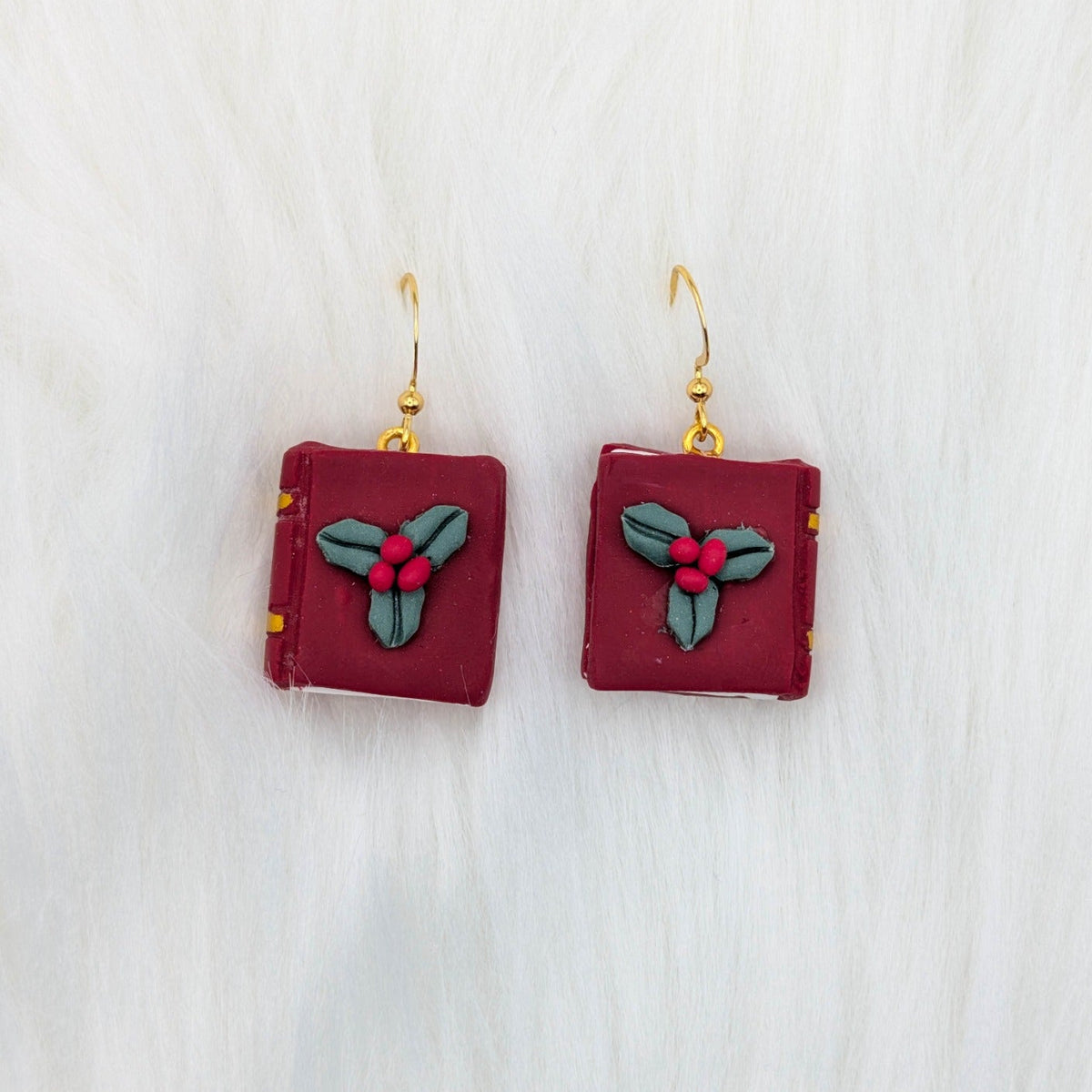 Burgundy miniature book earrings decorated with holly leaves and berries, with gold-tone hooks.