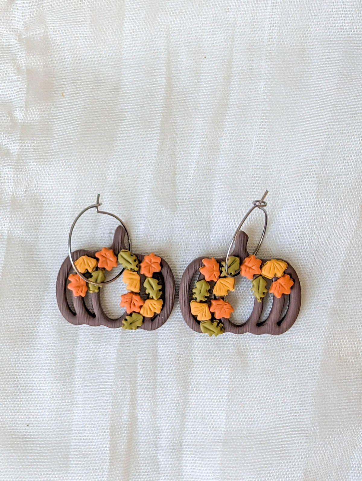 Close-up of brown pumpkin wreath earrings with autumn leaves and surgical-grade stainless steel hoops