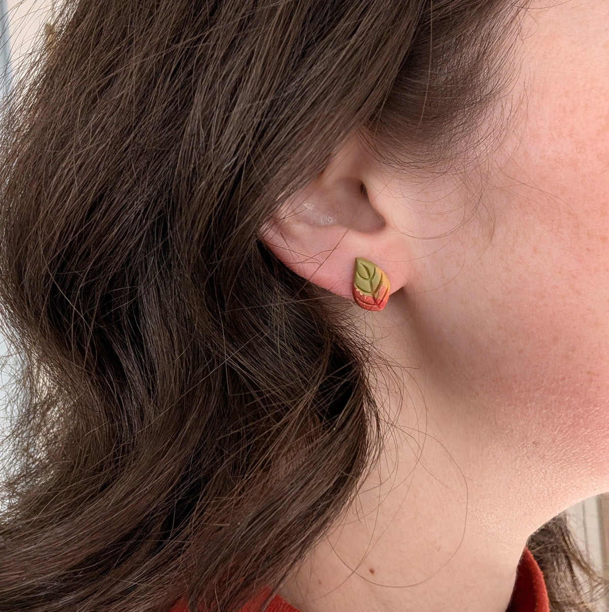 Green autumn leaf stud earring with copper accents worn on ear