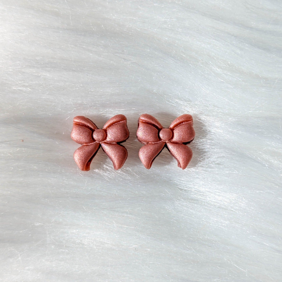 Rose gold polymer clay bow stud earrings on a soft white background