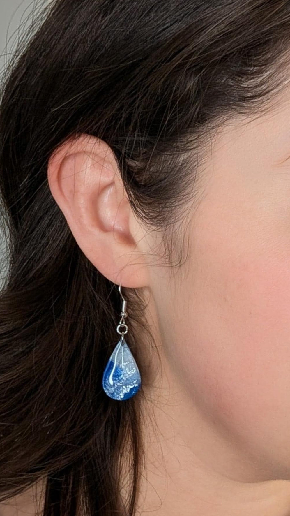 Woman wearing a blue teardrop earring with a neutral background