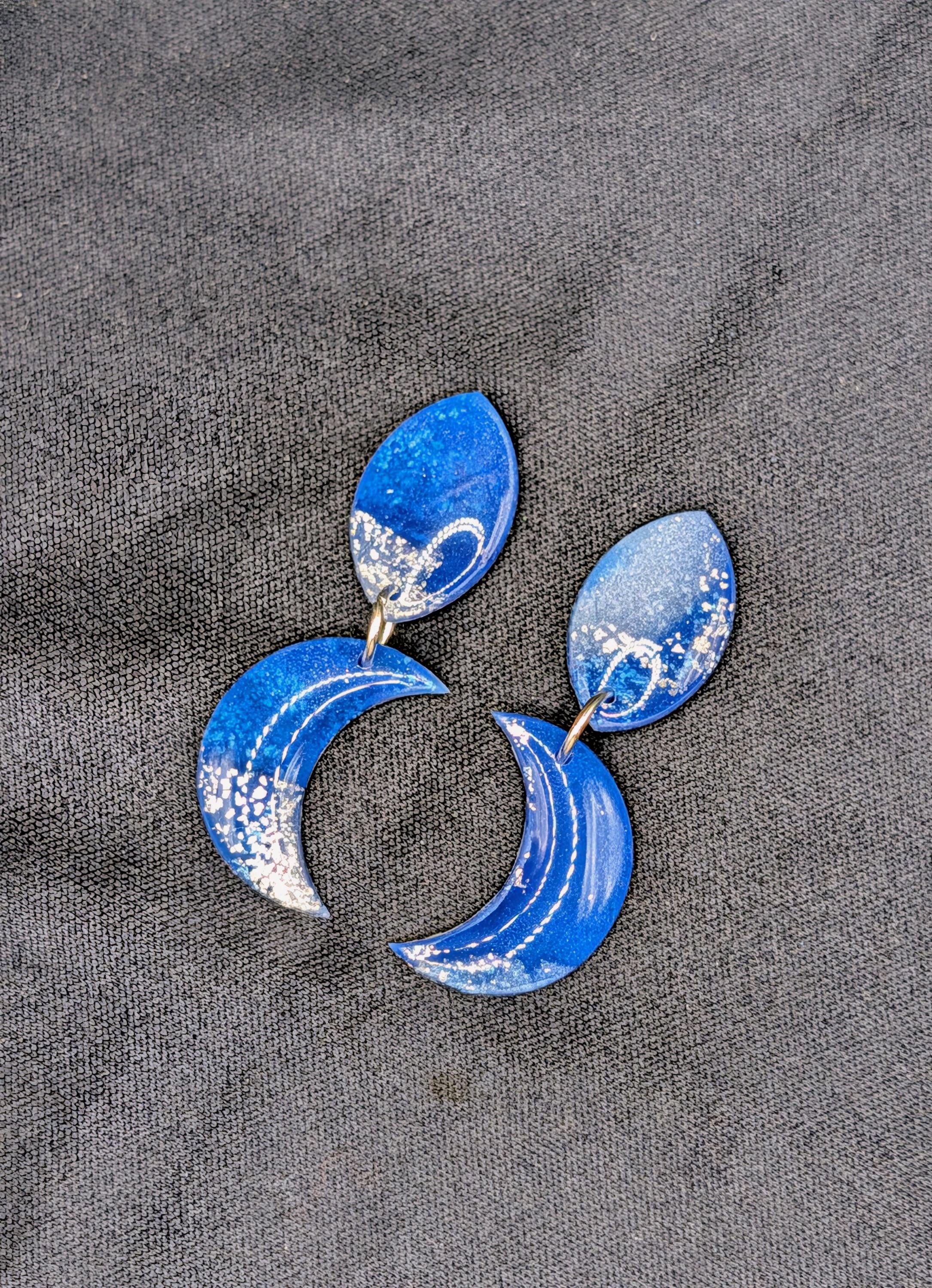 Blue crescent moon earrings on a gray fabric background