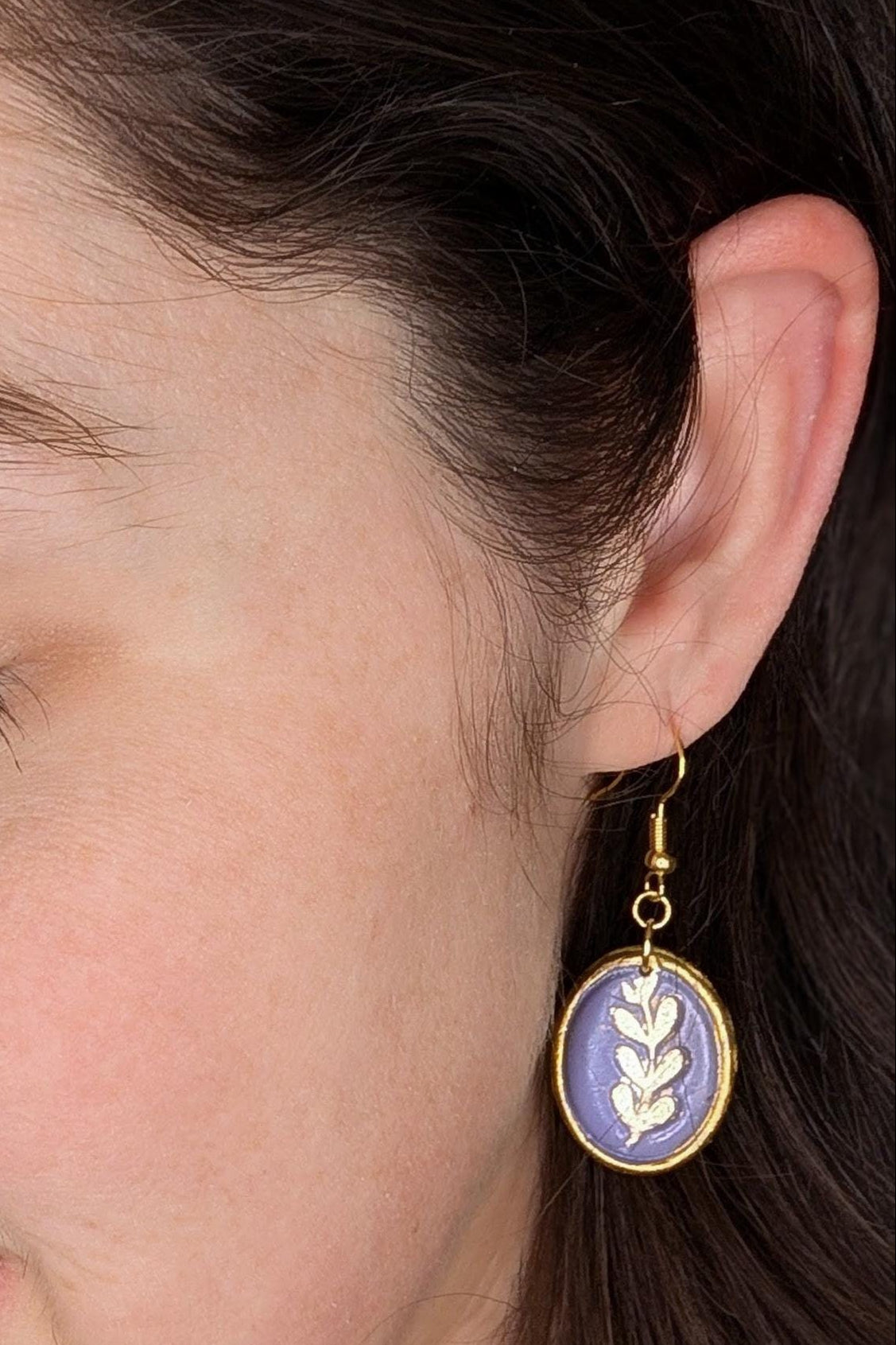 Close-up of a woman wearing gold earrings with purple stones.