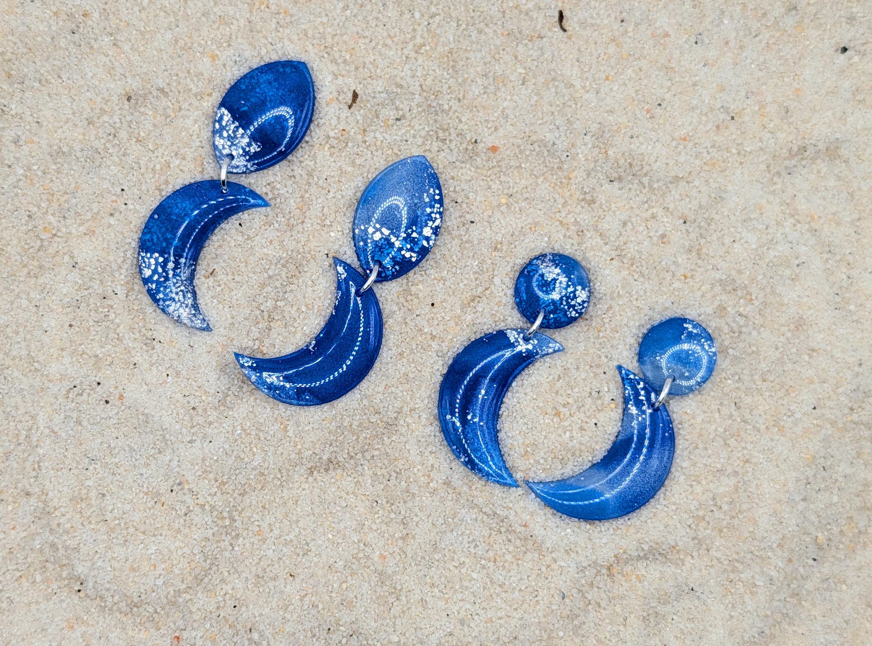Blue hoop earrings with star-like embellishments on a sandy surface