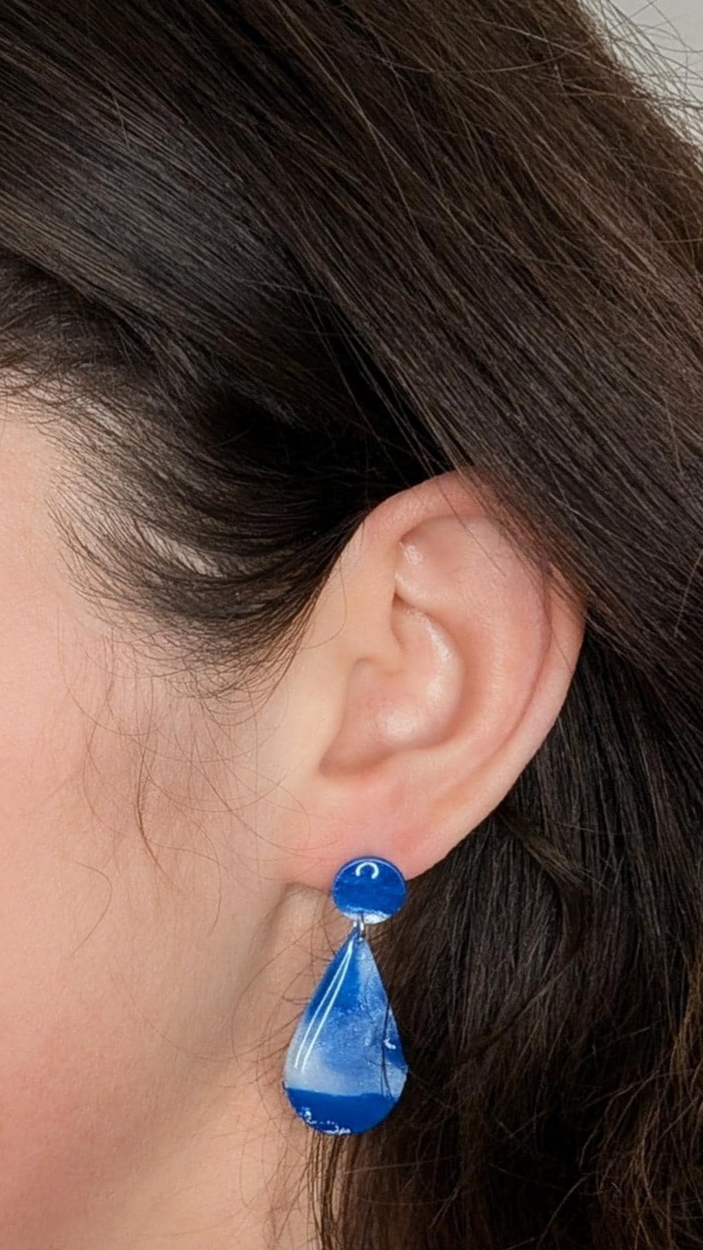 Close-up of a woman wearing blue teardrop earrings against a neutral background