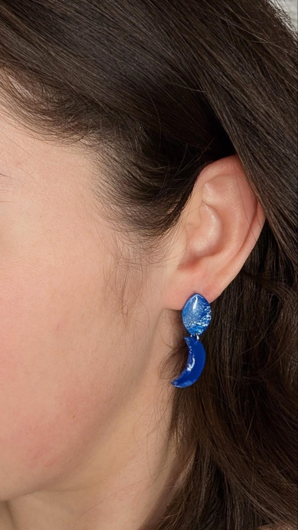 Close-up of a person wearing blue earrings with a neutral background