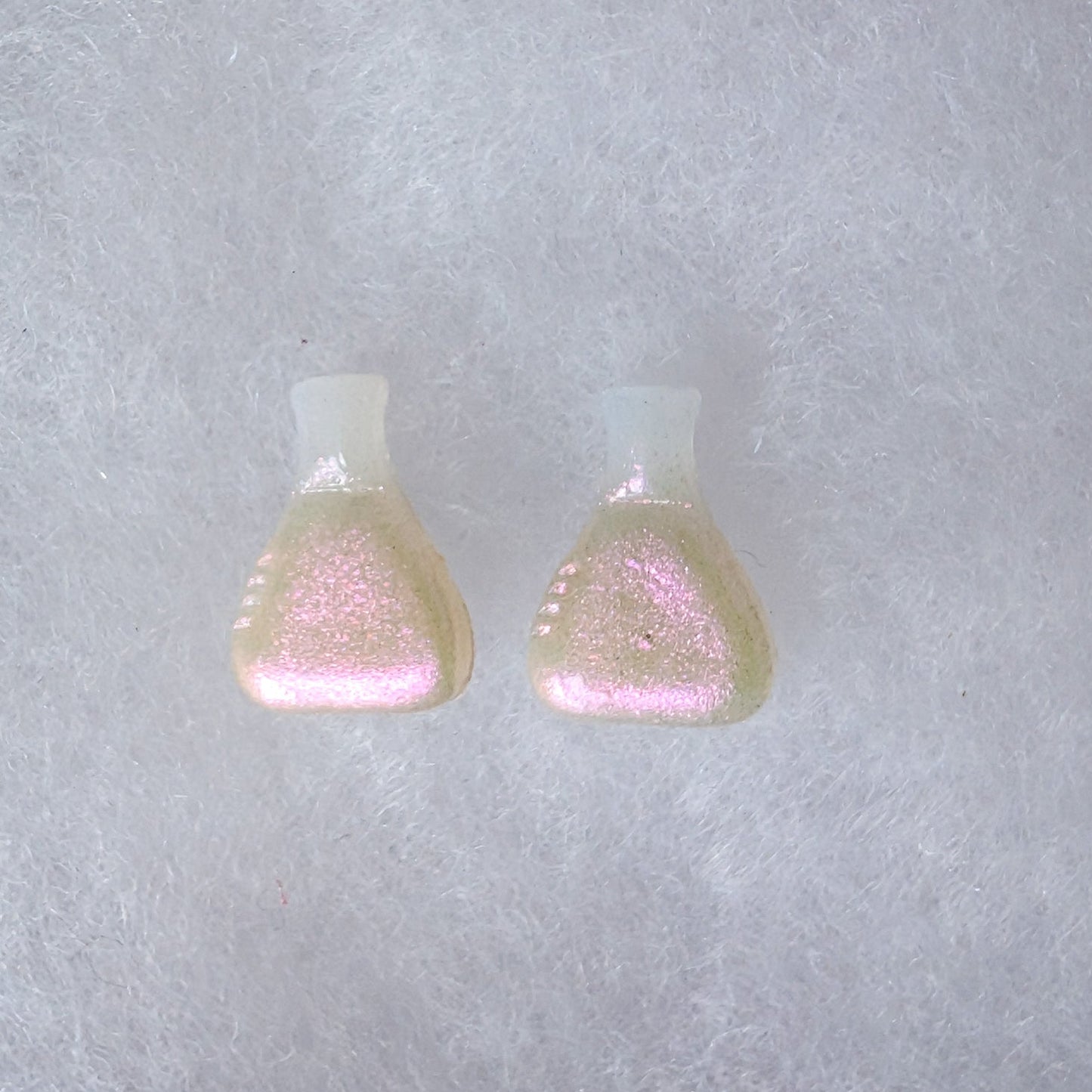 A pair of beaker shaped stud earrings with a translucent top and a glittery gold to pink colorshift finish.