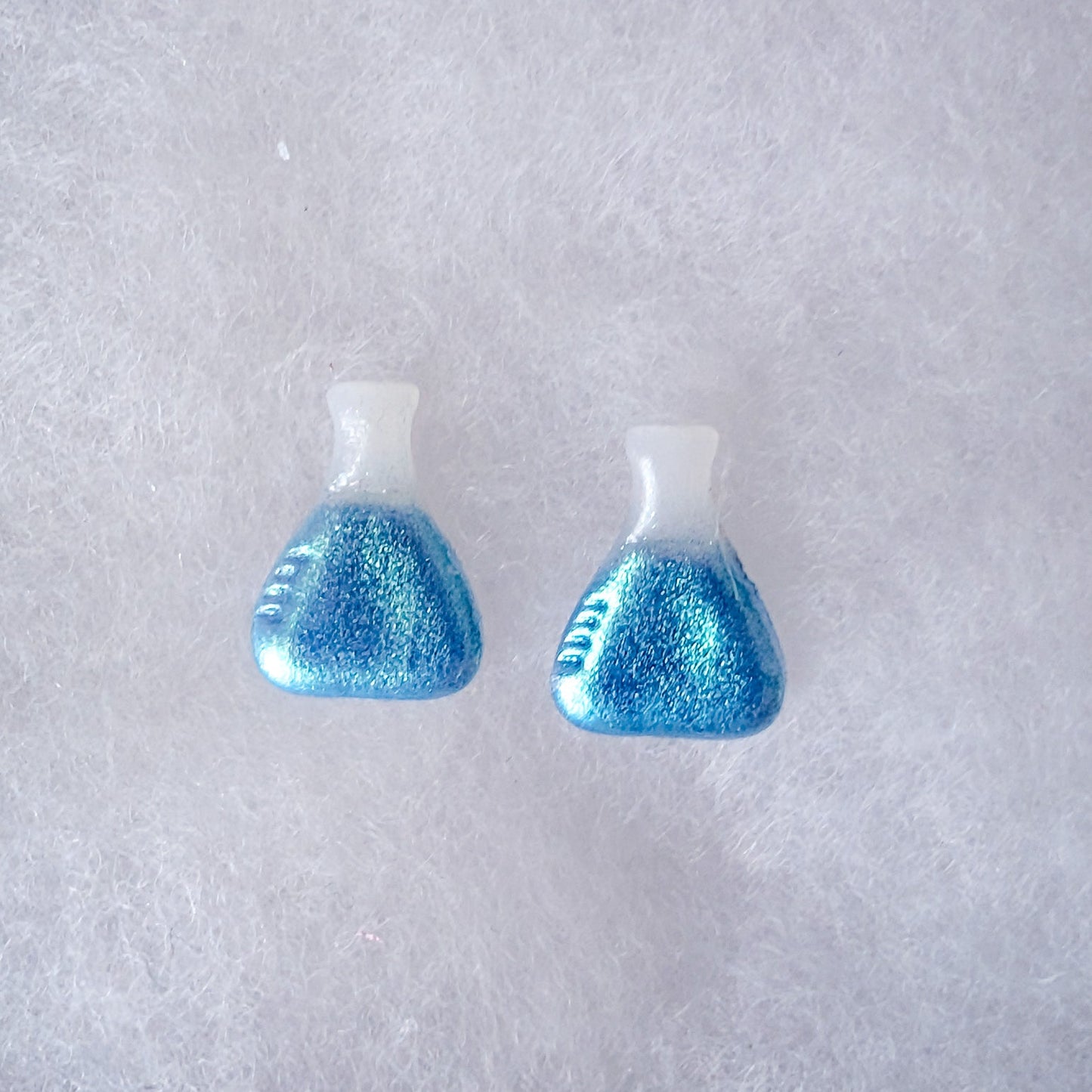 A pair of beaker shaped stud earrings with a translucent top and a glittery blue to green colorshift finish.