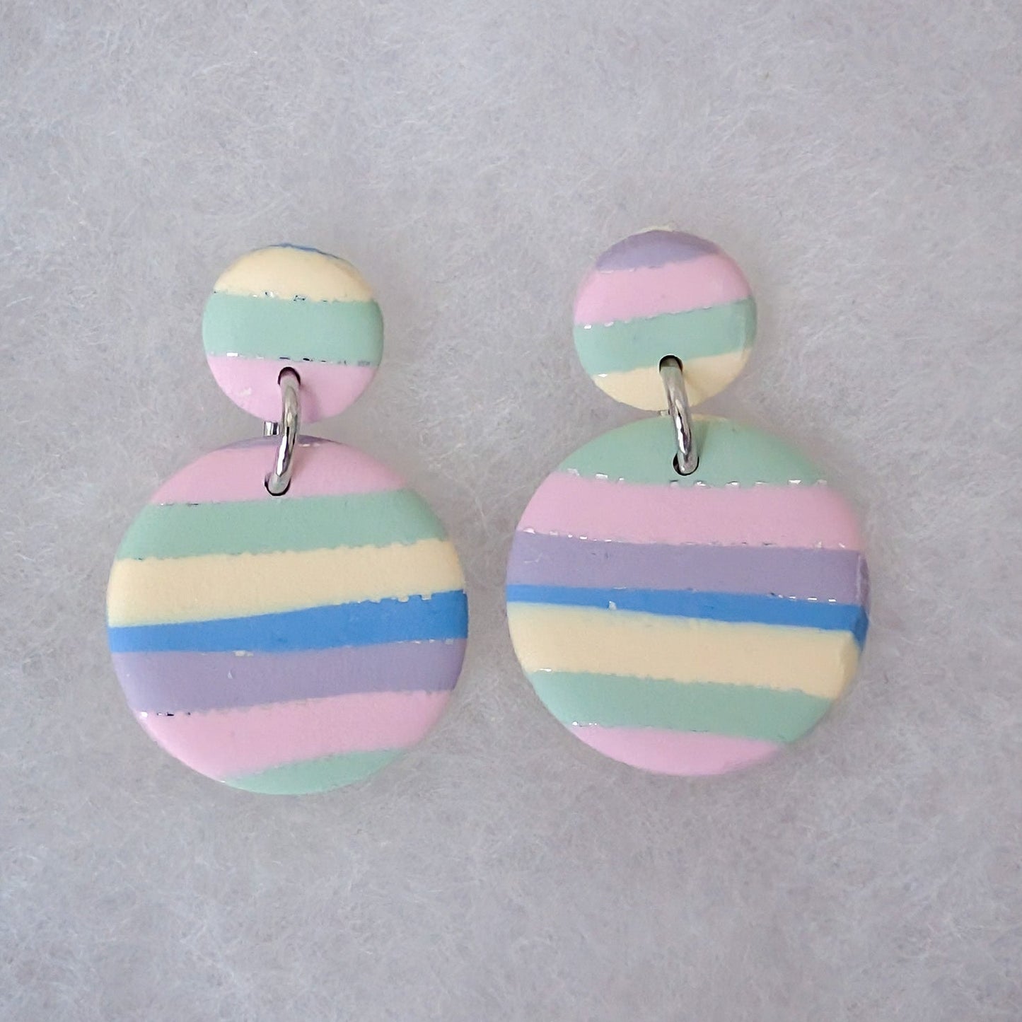 A pair of pastel striped dangle earrings with a small round top piece connected by a silver jump ring to a larger circular drop. The earrings feature horizontal stripes in pink, light blue, mint green, lavender, and cream.