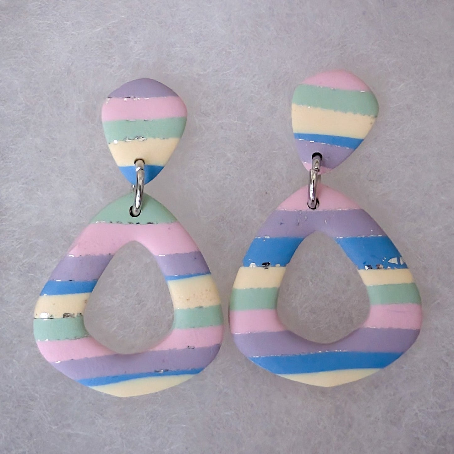 A pair of handmade hollow diamond teardrop shaped drop earrings with a colorful pastel striped pattern, featuring a small oval top and silver-tone jump rings.