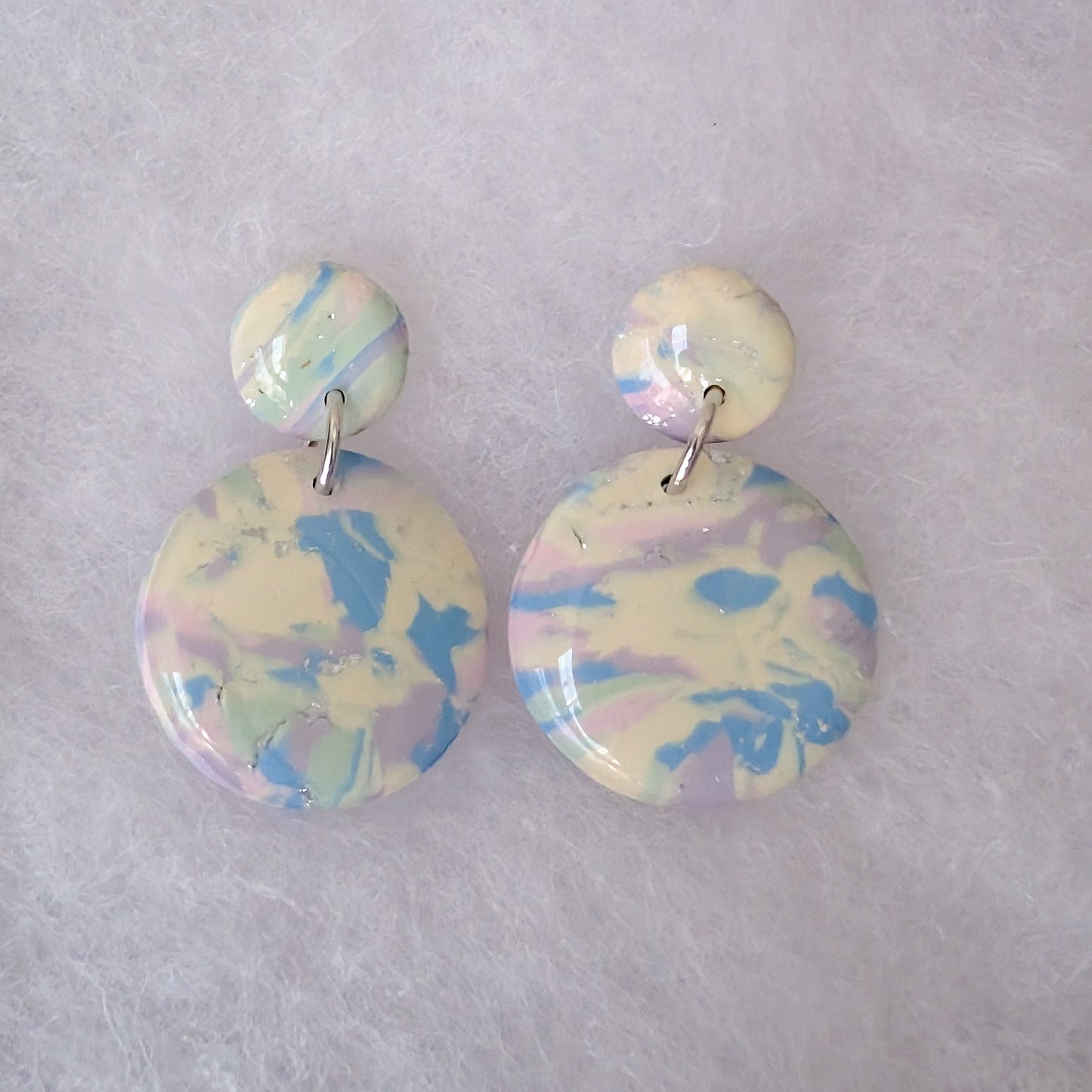 A pair of drop earrings with small round studs and larger marbled oval drops in pastel cream, blue, and lavender.
