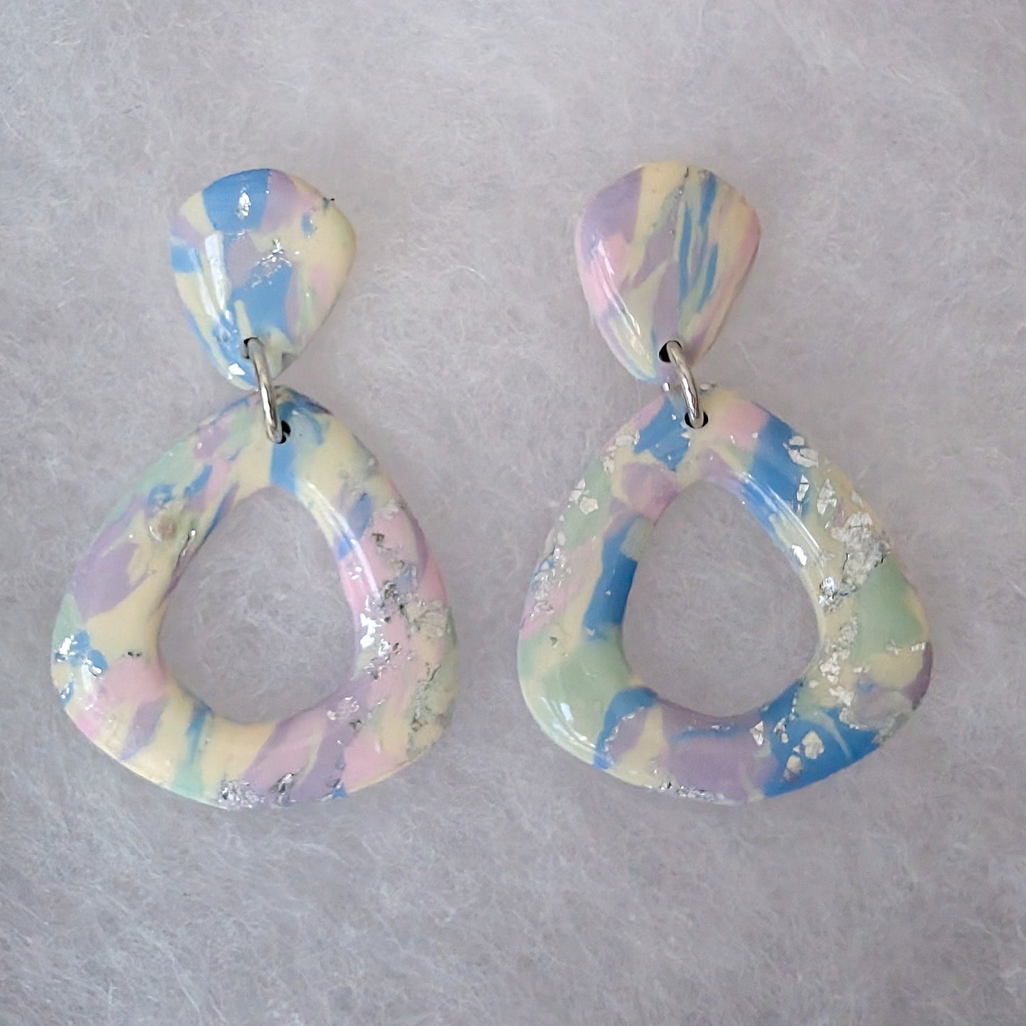 A pair of dangling geometric earrings with a marbled pastel pattern of blue, pink, yellow, and white, accented with small silver glitter flakes.