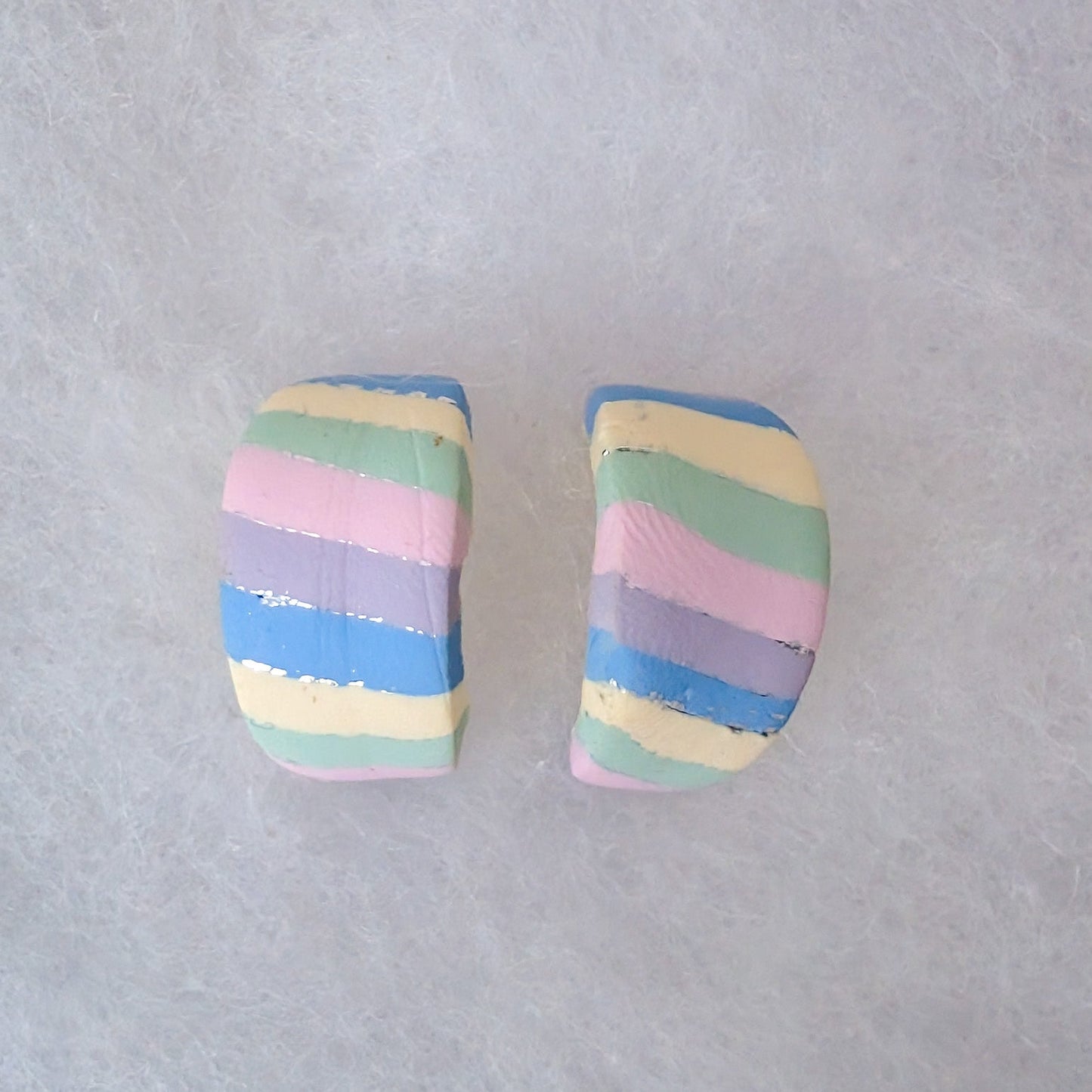 Two small huggie earrings with horizontal pastel stripes in blue, pink, yellow, green, and purple.