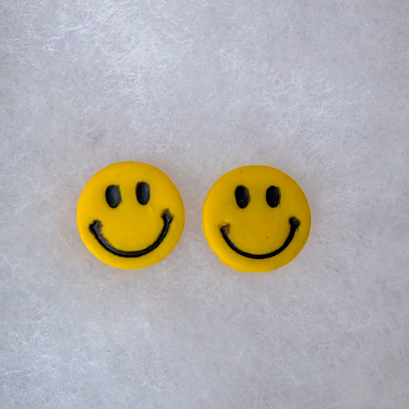 A pair of yellow smiley face stud earrings with black eyes and curved smiles.