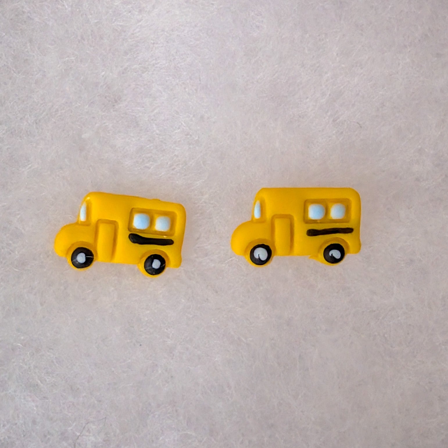 A pair of yellow school bus stud earrings with black wheels and white windows.