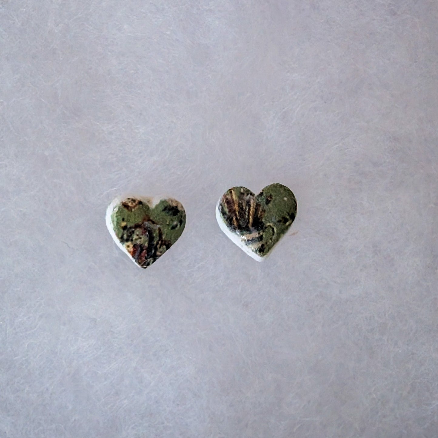 A pair of small heart-shaped stud earrings with a green and brown marbled pattern.
