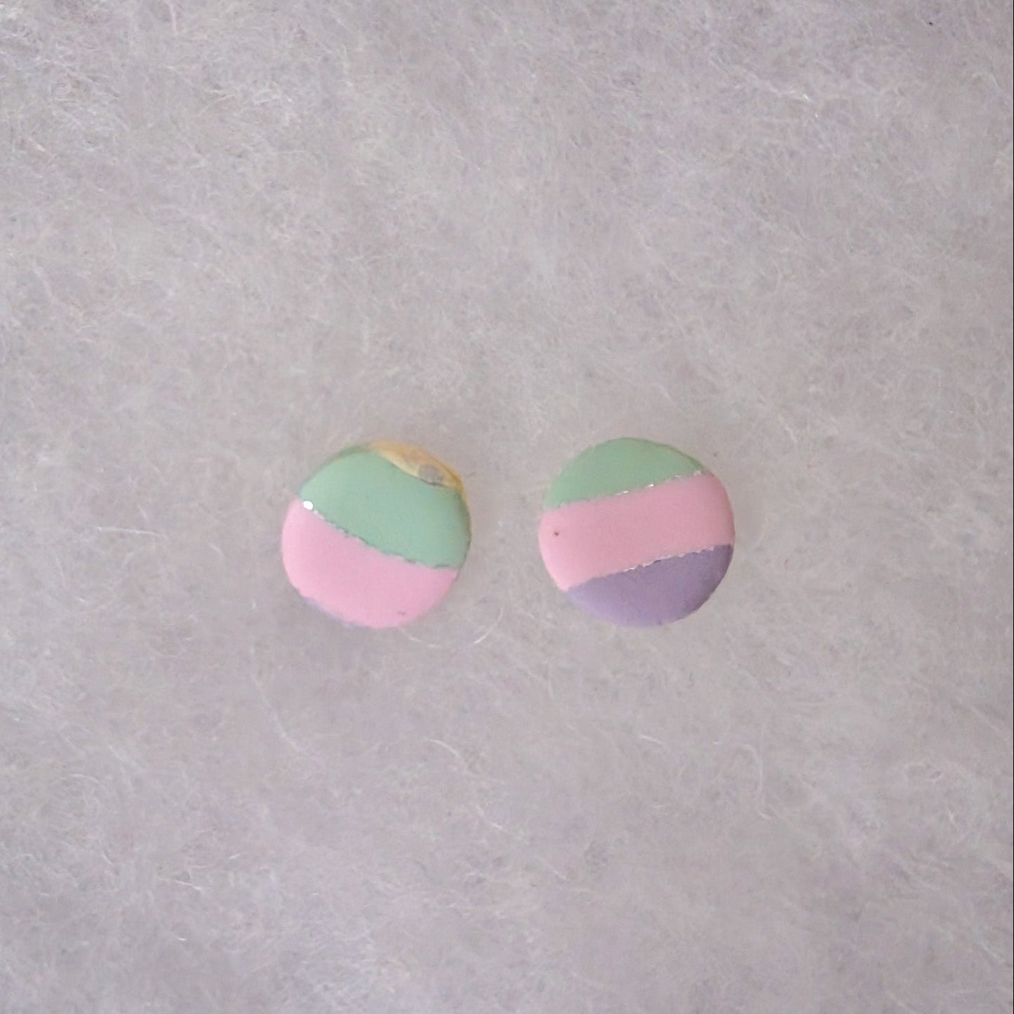 A pair of round stud earrings with a pastel three-color design of pink, mint green, and lavender purple with silver accents