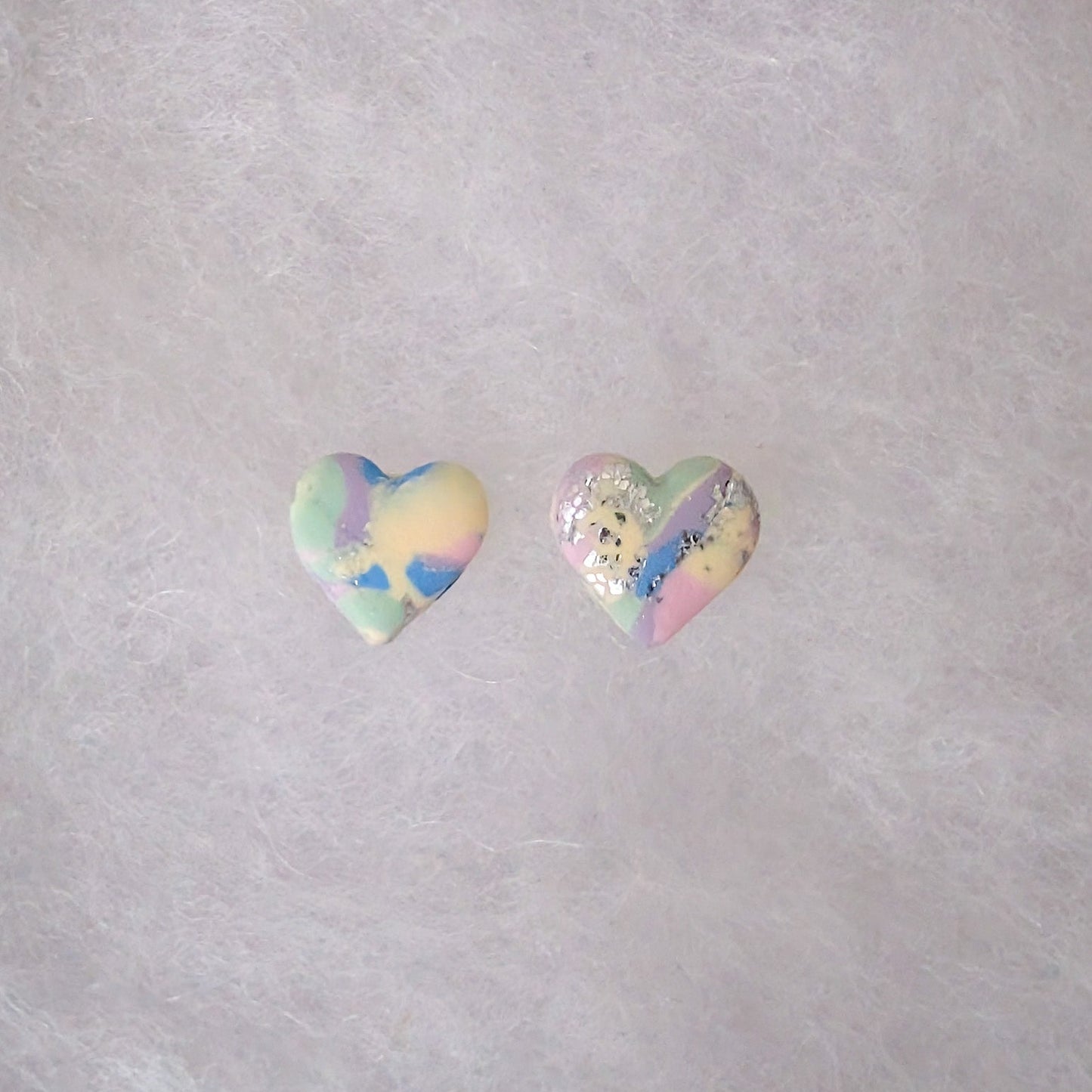 Two small heart-shaped stud earrings with a pastel tie-dye pattern and silver accents.