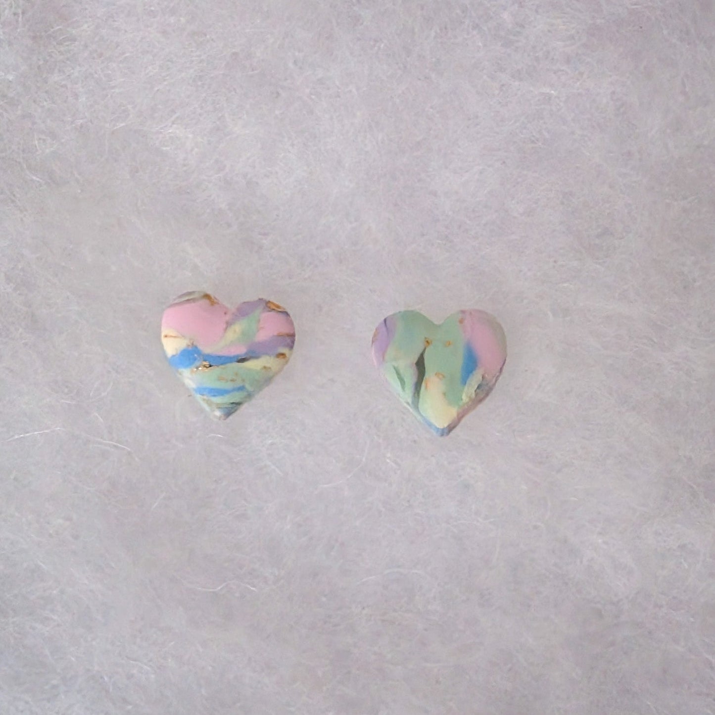 Two small heart-shaped stud earrings with a pastel marbled pattern of pink, blue, green, and yellow with gold accents