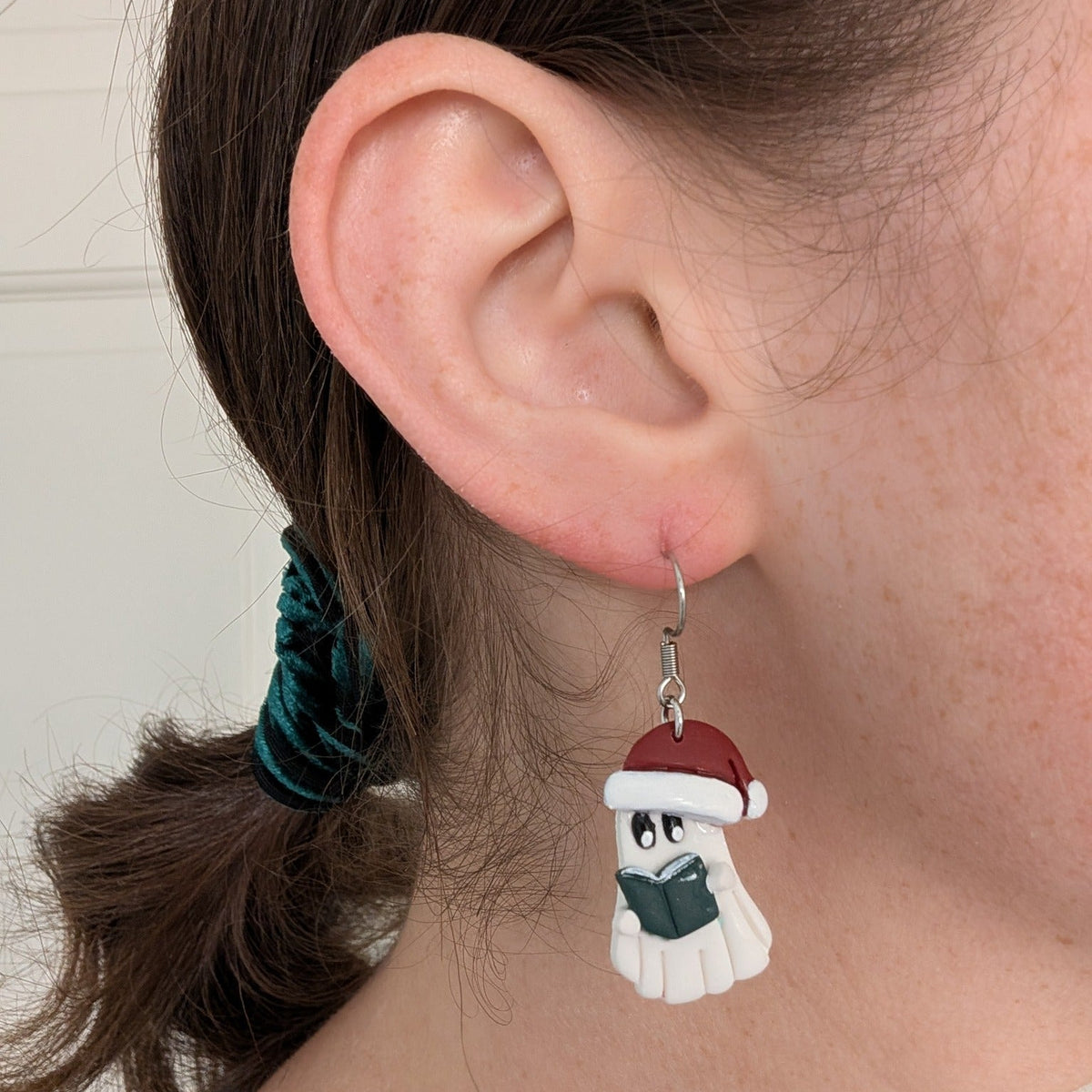 Santa ghost reader earring worn on ear, showing the book detail and scale