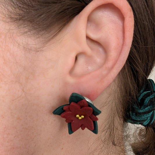 Poinsettia statement stud earring worn on ear, showing its size and dark green leaves