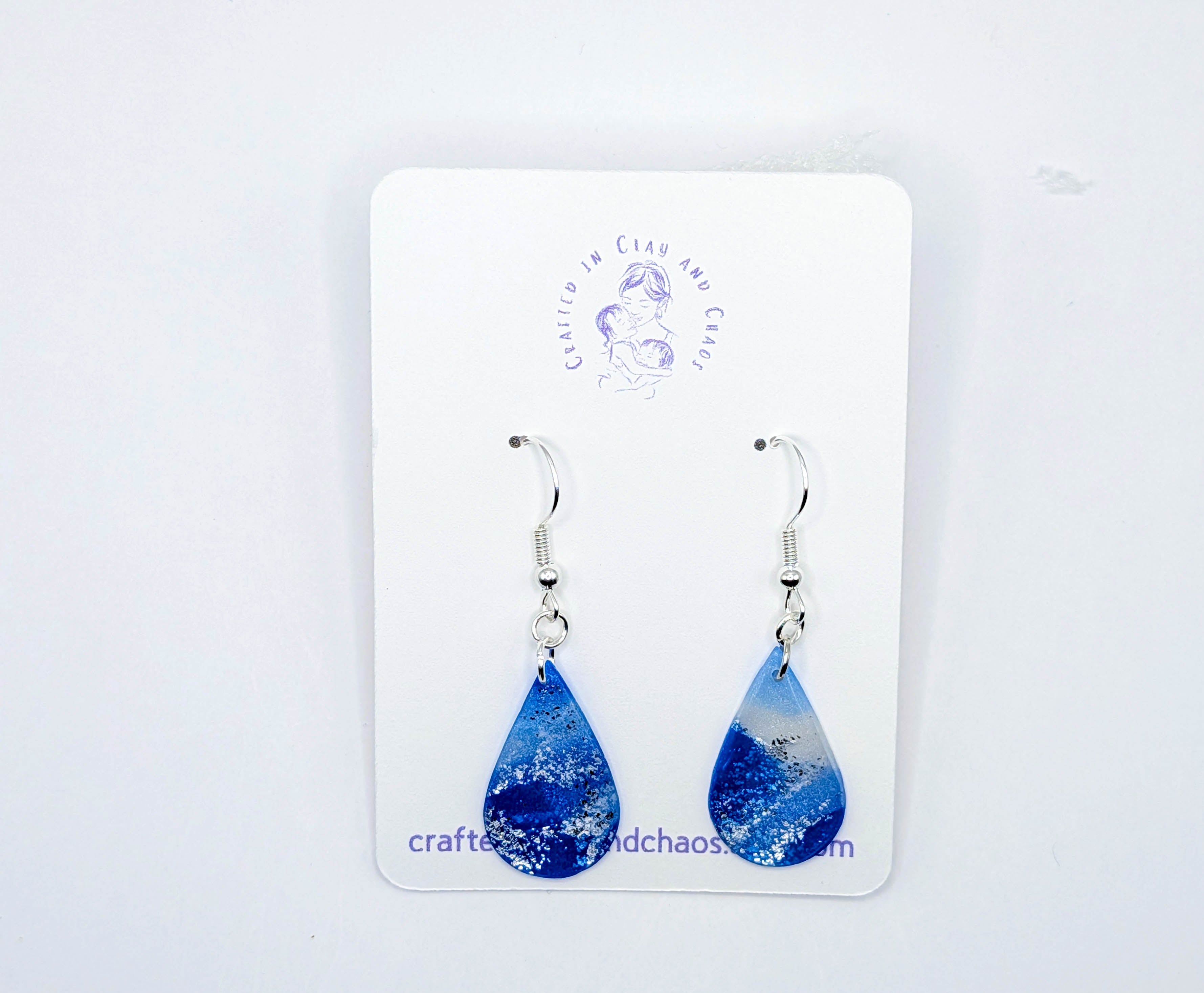 Blue teardrop earrings on a white card with 'Crafted with Chaos' branding.