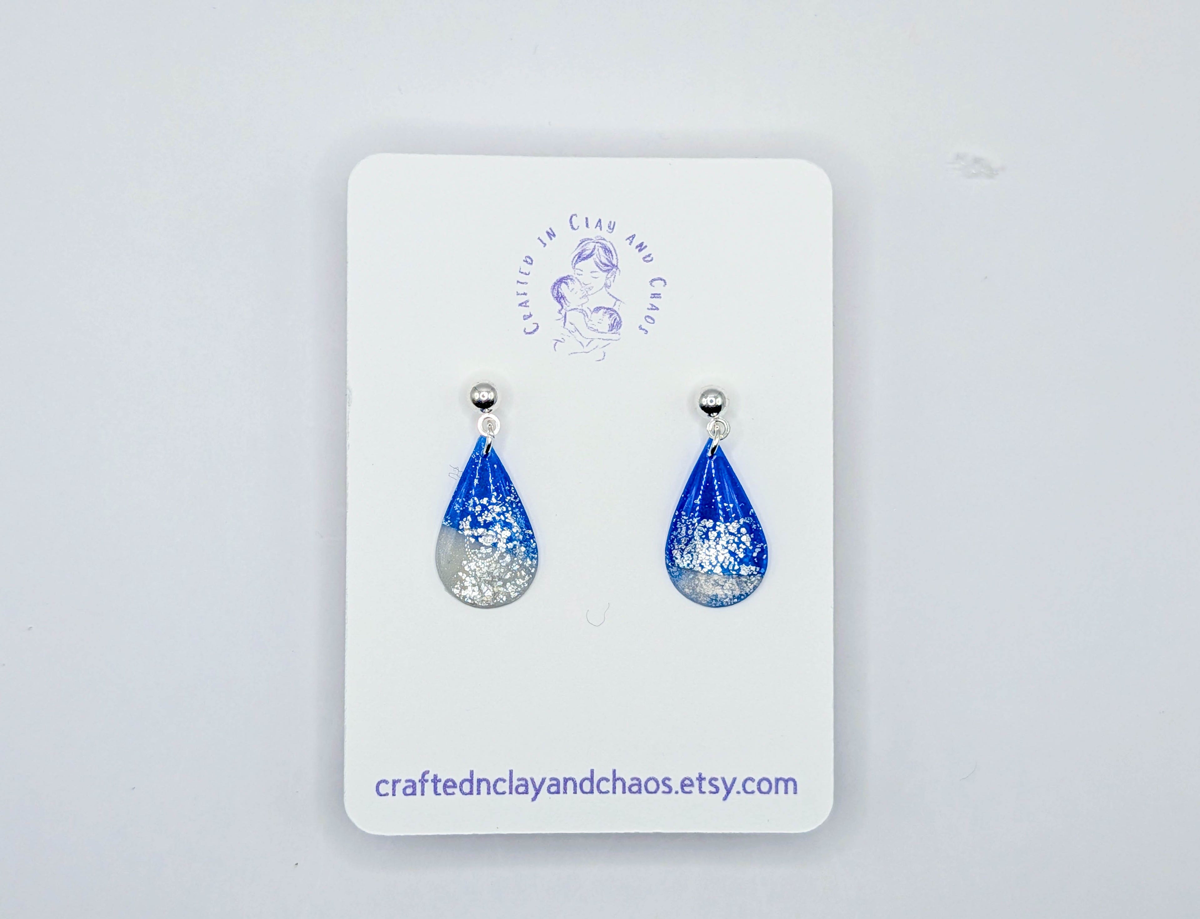 Blue teardrop earrings on a white card with a brand logo, against a light gray background.