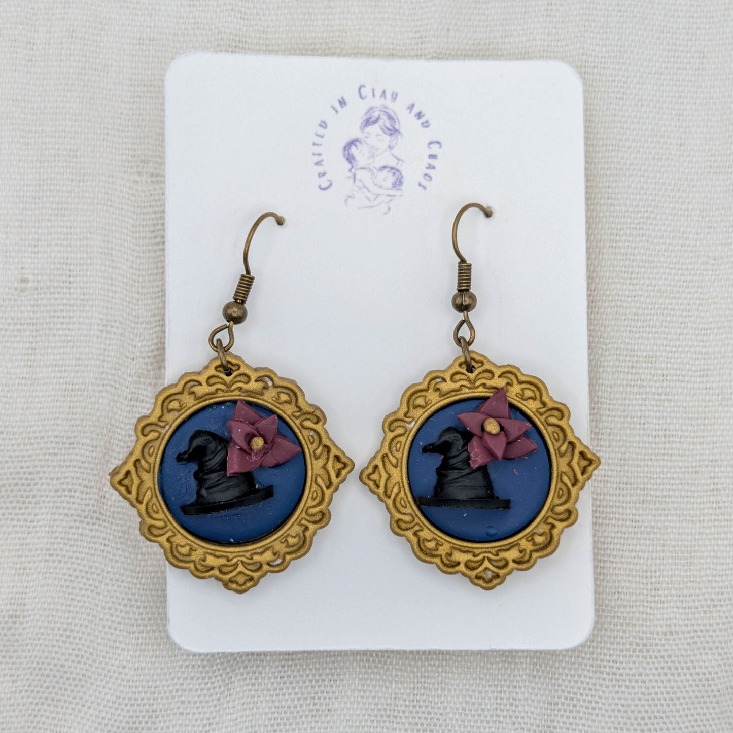 Antique gold round vintage frame earrings with blue background, black witch hats, burgundy flowers, and bronze-tone hooks