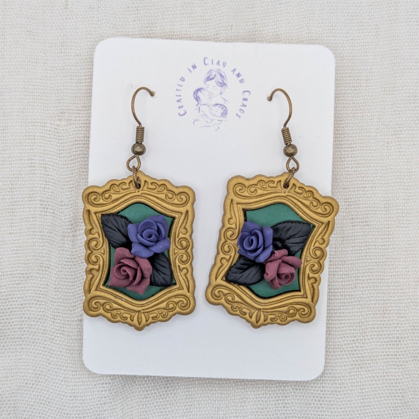 Antique gold vintage frame earrings with forest green background, sculpted purple and burgundy roses, black leaves, and bronze-tone hooks