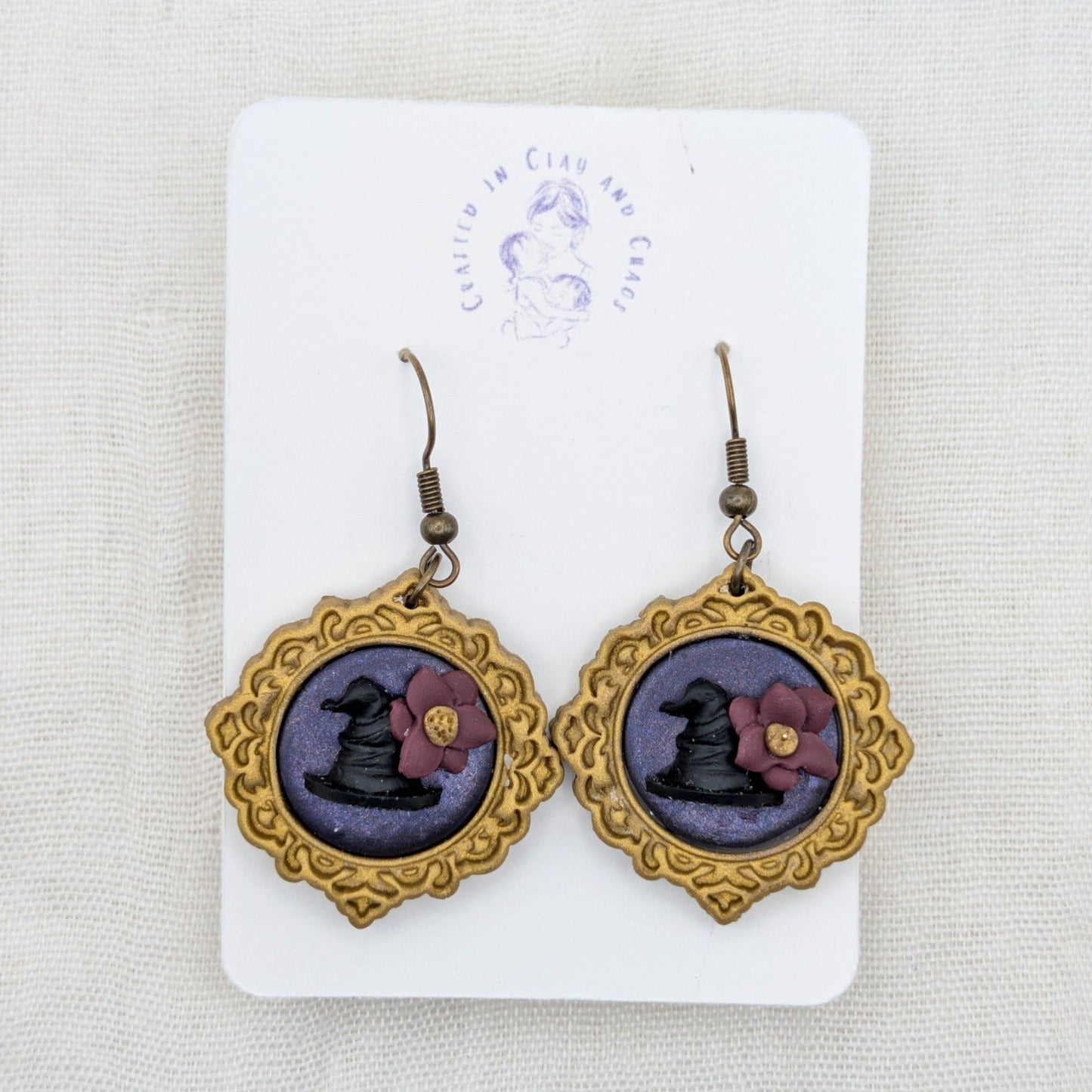 Antique gold round vintage frame earrings with purple shimmer background, black witch hats, burgundy flowers, and bronze-tone hooks
