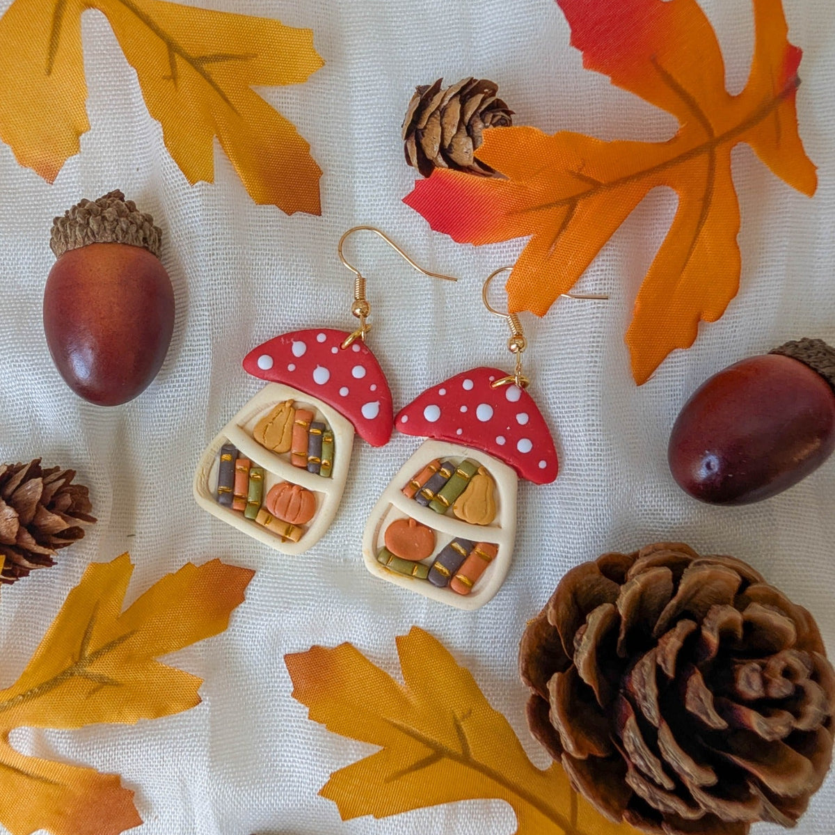 Handmade autumn mushroom bookcase earrings with tiny books, pumpkins, gourds, fall leaves, acorns, and pinecones