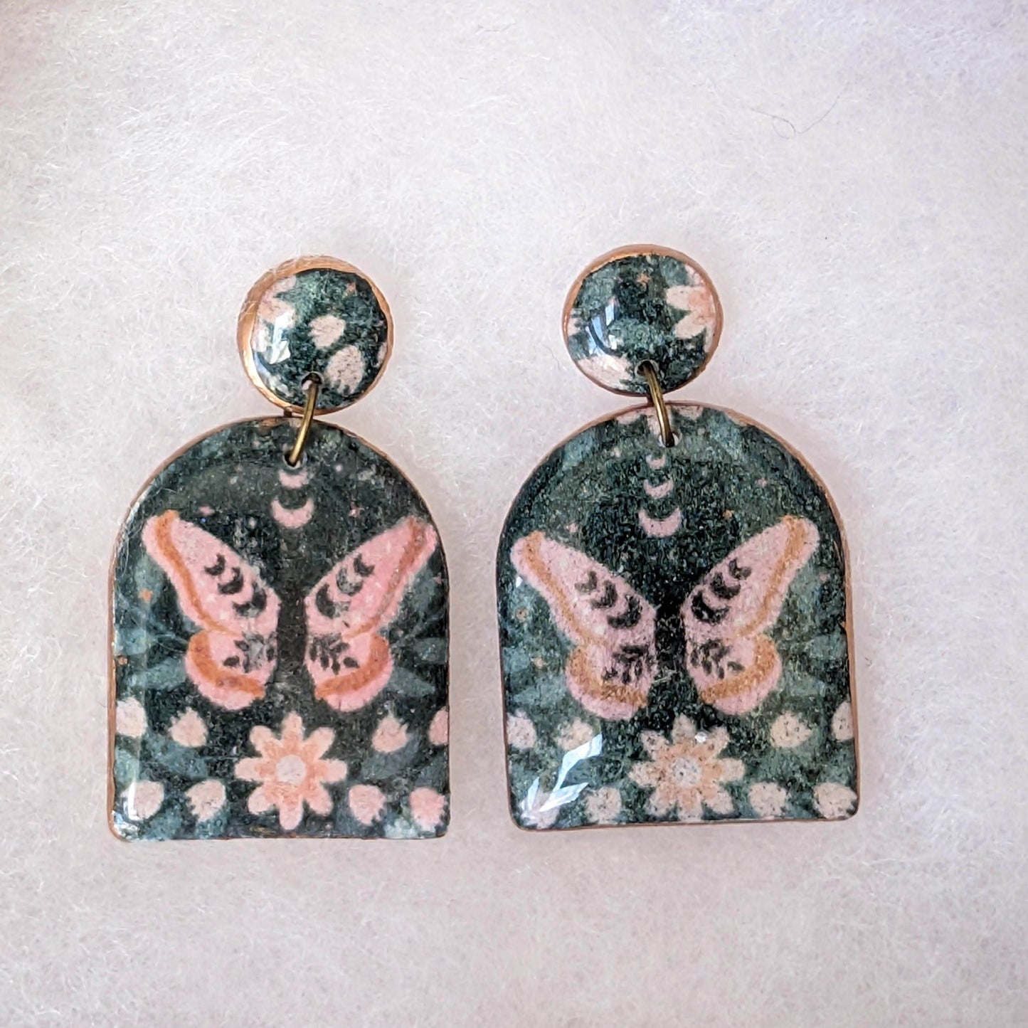 Black moth arch earrings with dusty pink flowers, moon phases, and glossy resin topcoat