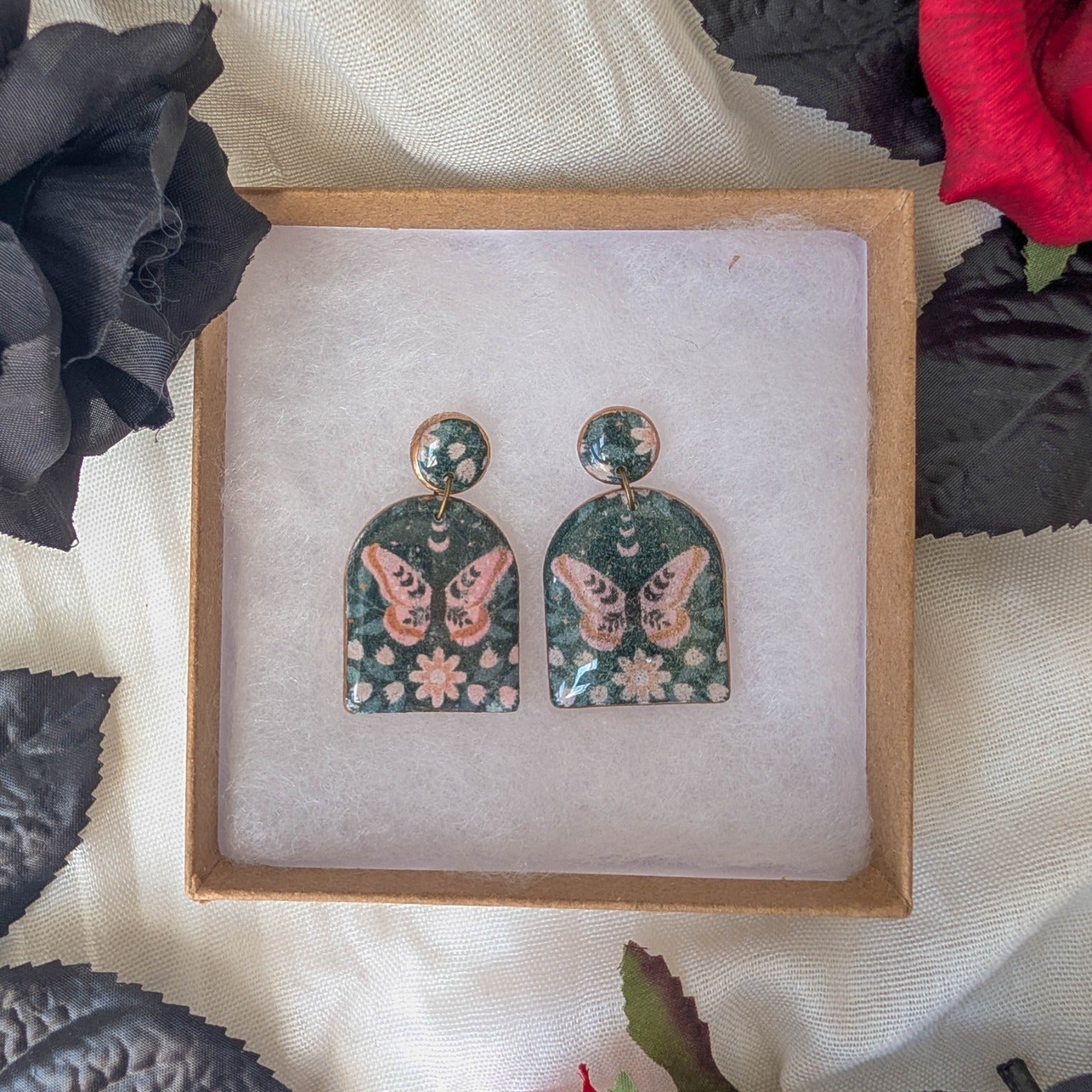 Black moth arch earrings with dusty pink flowers and copper accents in a gothic floral display