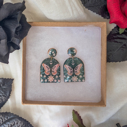 Black moth arch earrings with dusty pink flowers and copper accents in a gothic floral display