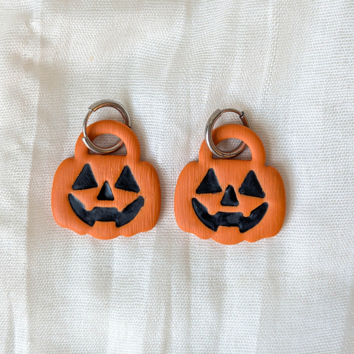 Orange trick-or-treat pumpkin earrings with black jack-o-lantern faces and silver-tone huggie hoops