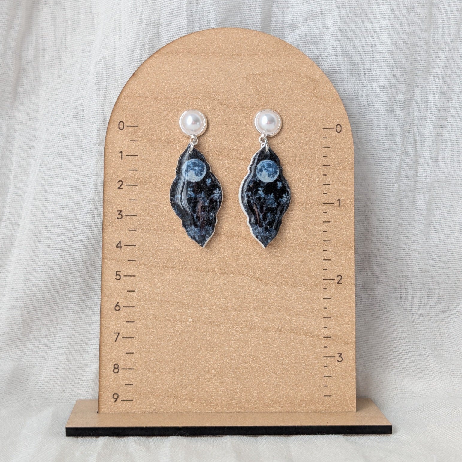 Blue moon petal earrings with faux pearl posts displayed beside a ruler